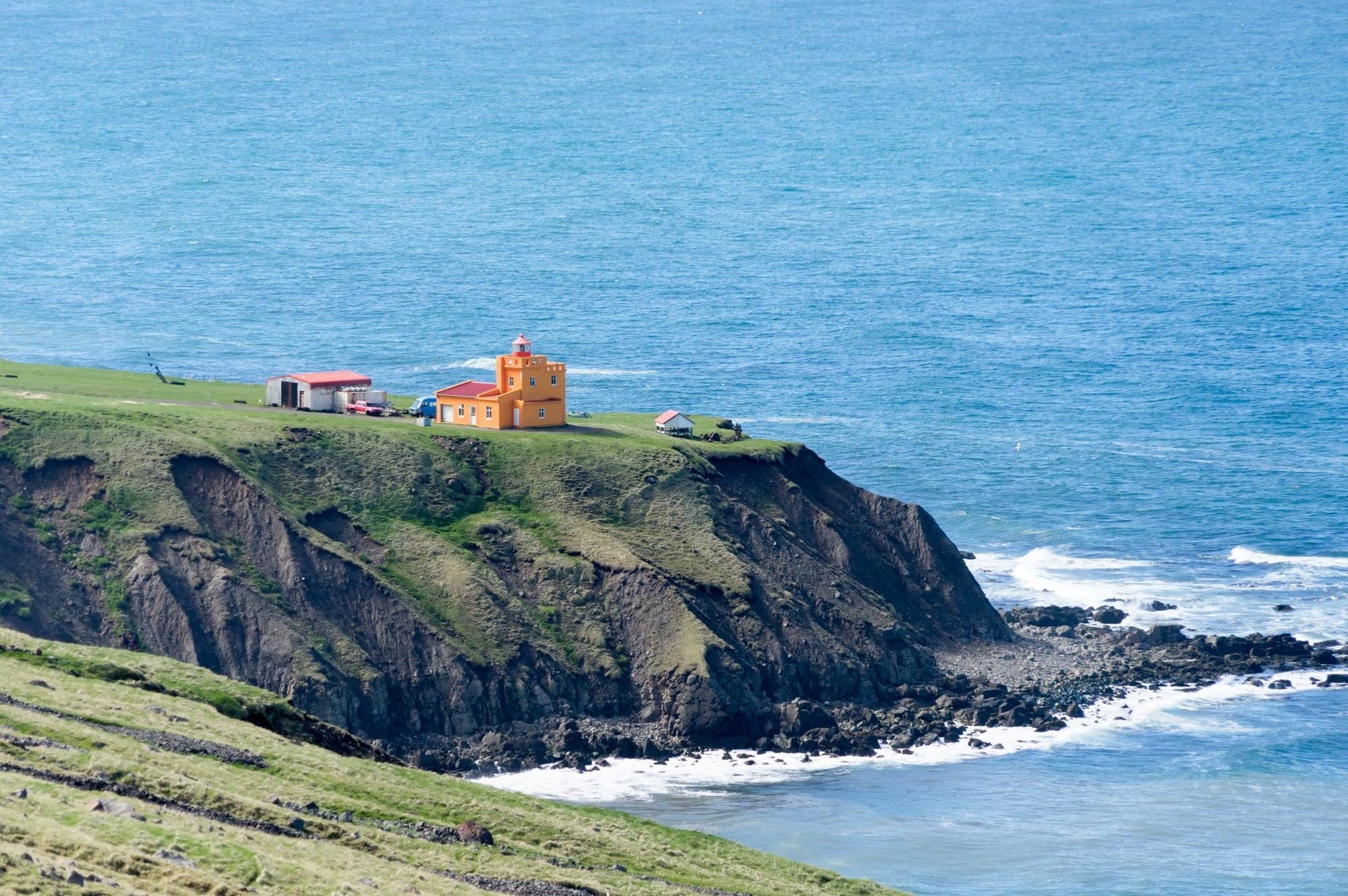 Sauðanesviti lighthouse on the Tröllaskagi coast with mountains beyond.