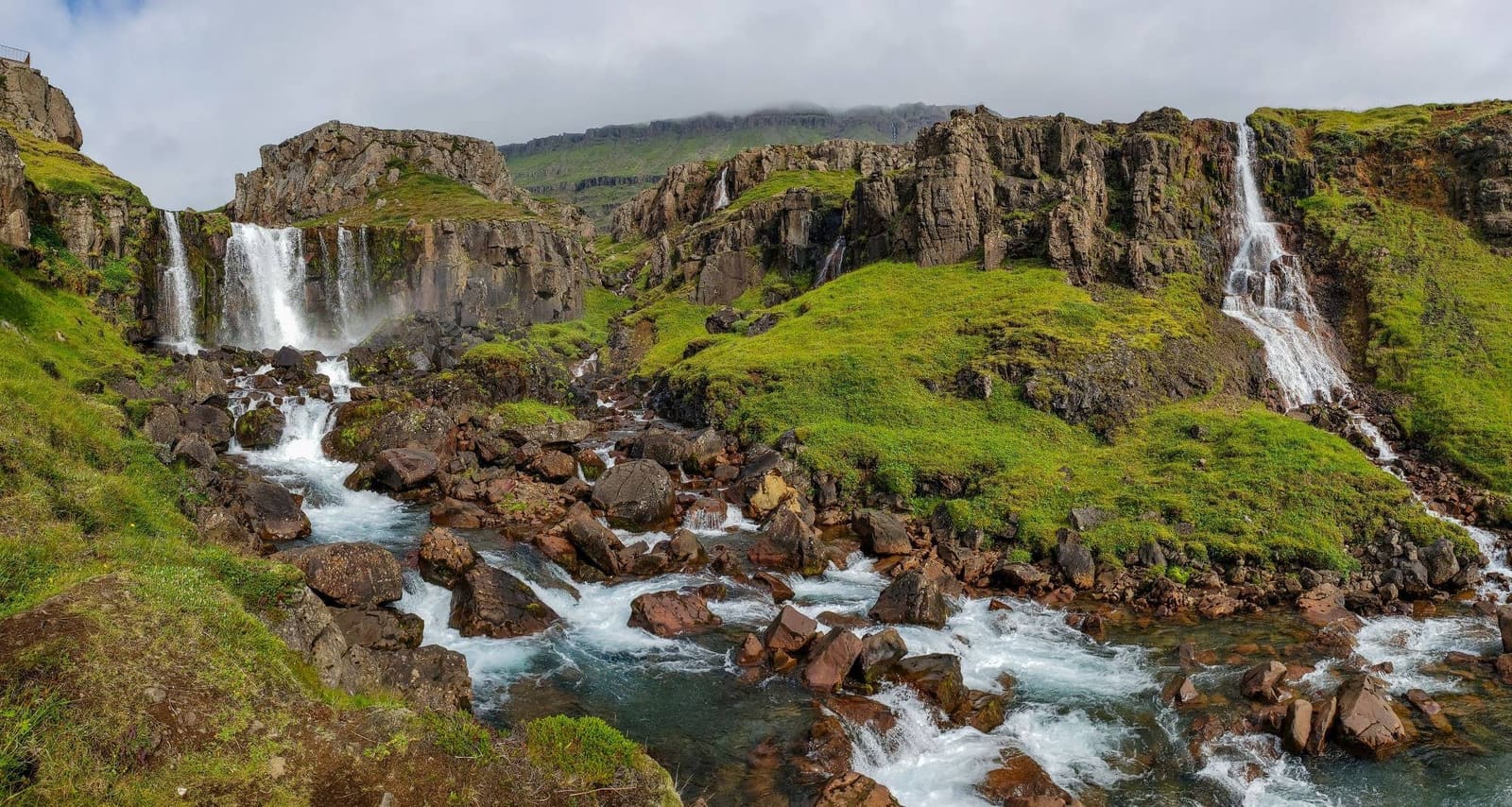 Vestdalsfossar cascades dropping through green rock ledges above Seyðisfjörður.
