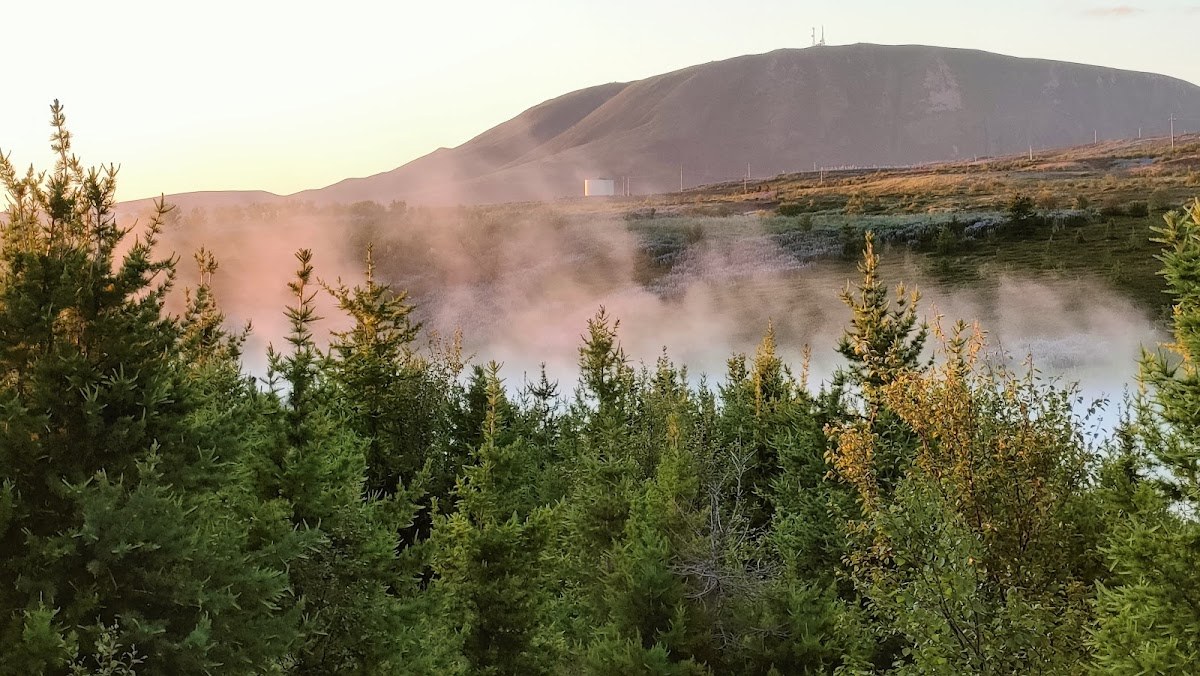 Steam rising from the Geothermal Goldfish Pond near Húsavík with a low mountain behind it.