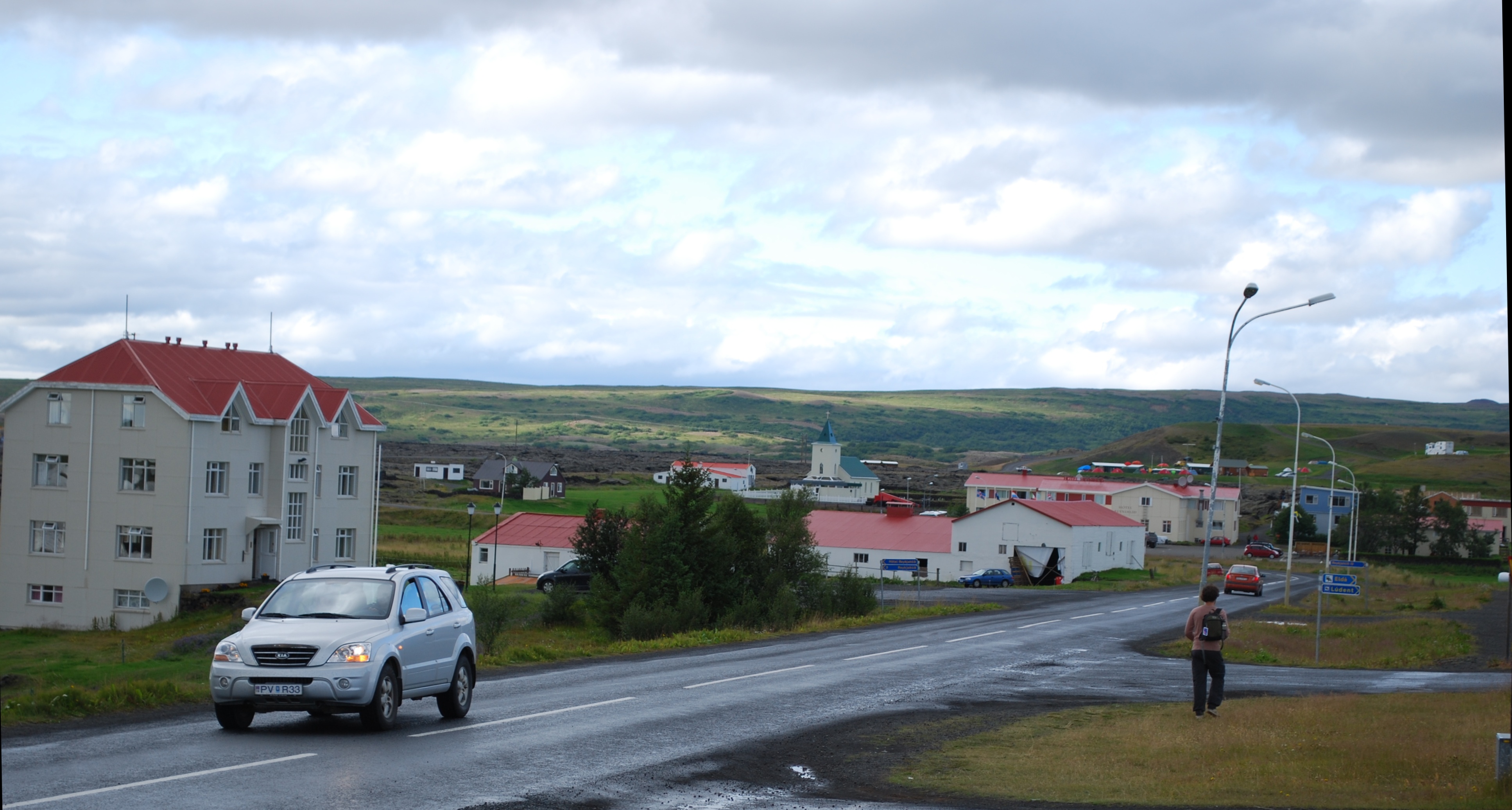 Road into Reykjahlíð with the church visible beyond houses and low green slopes.