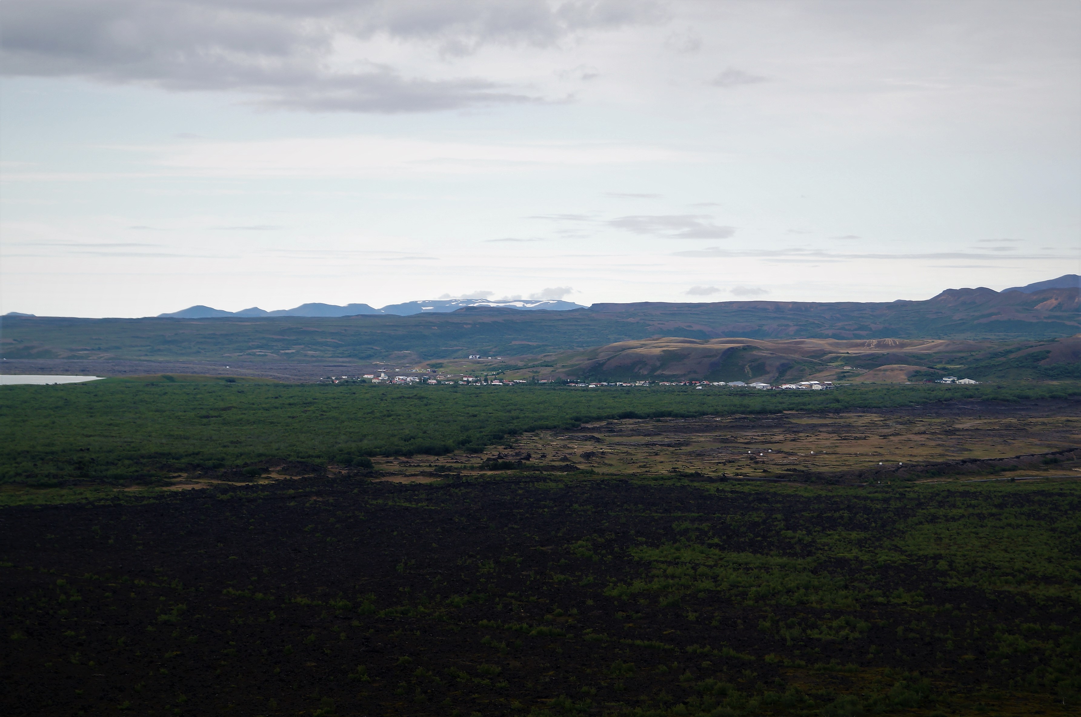 Reykjahlíð seen from Hverfjall as a small village beyond lava fields and low green scrub.
