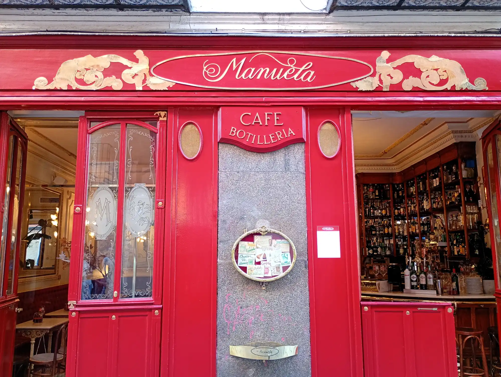 The bright red facade of Café Manuela in Madrid, with ornate gold lettering and a view into the bar area.