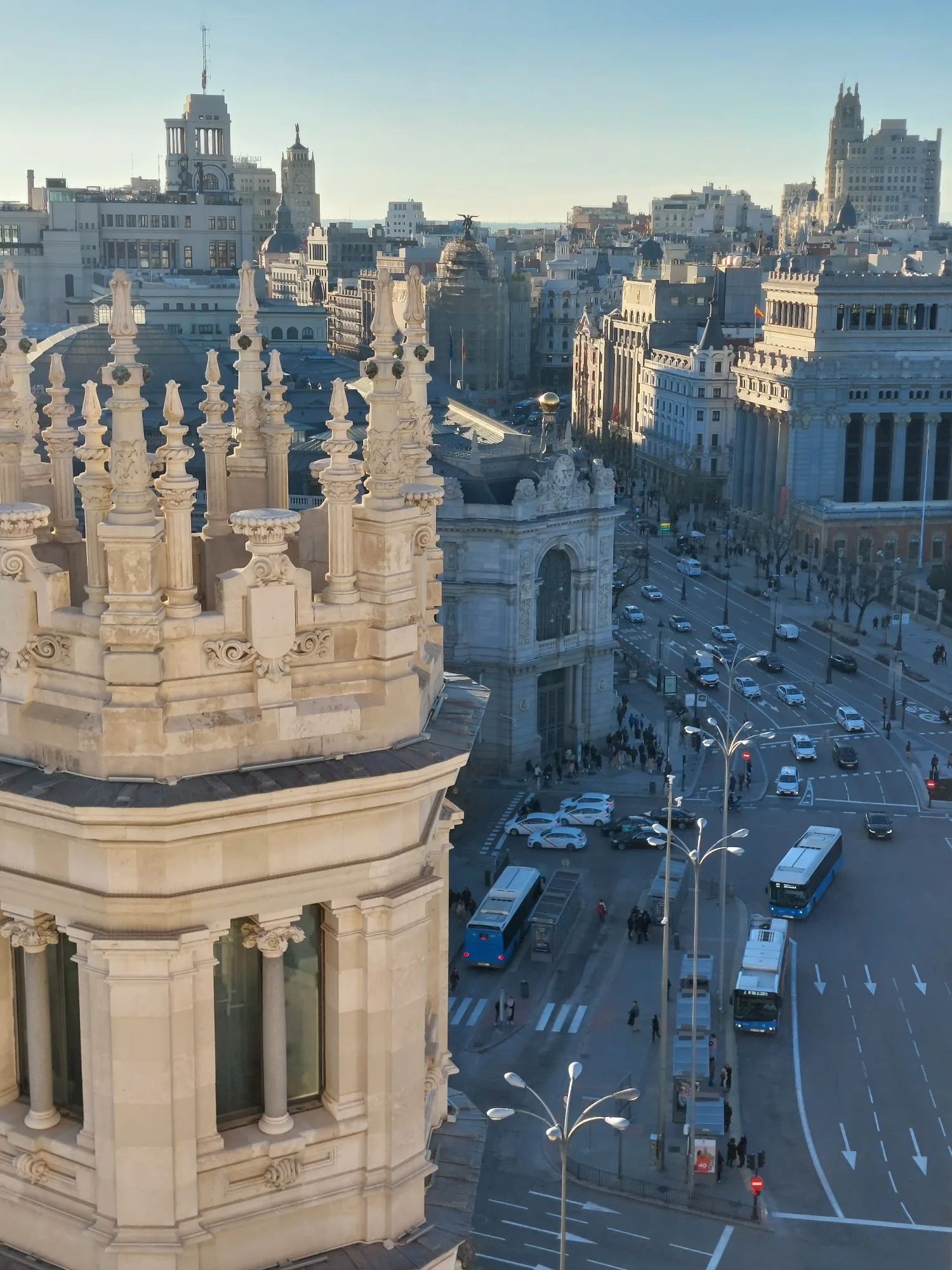 High-angle view of Calle de Alcalá in Madrid, with ornate stone spires in the foreground and city traffic below.