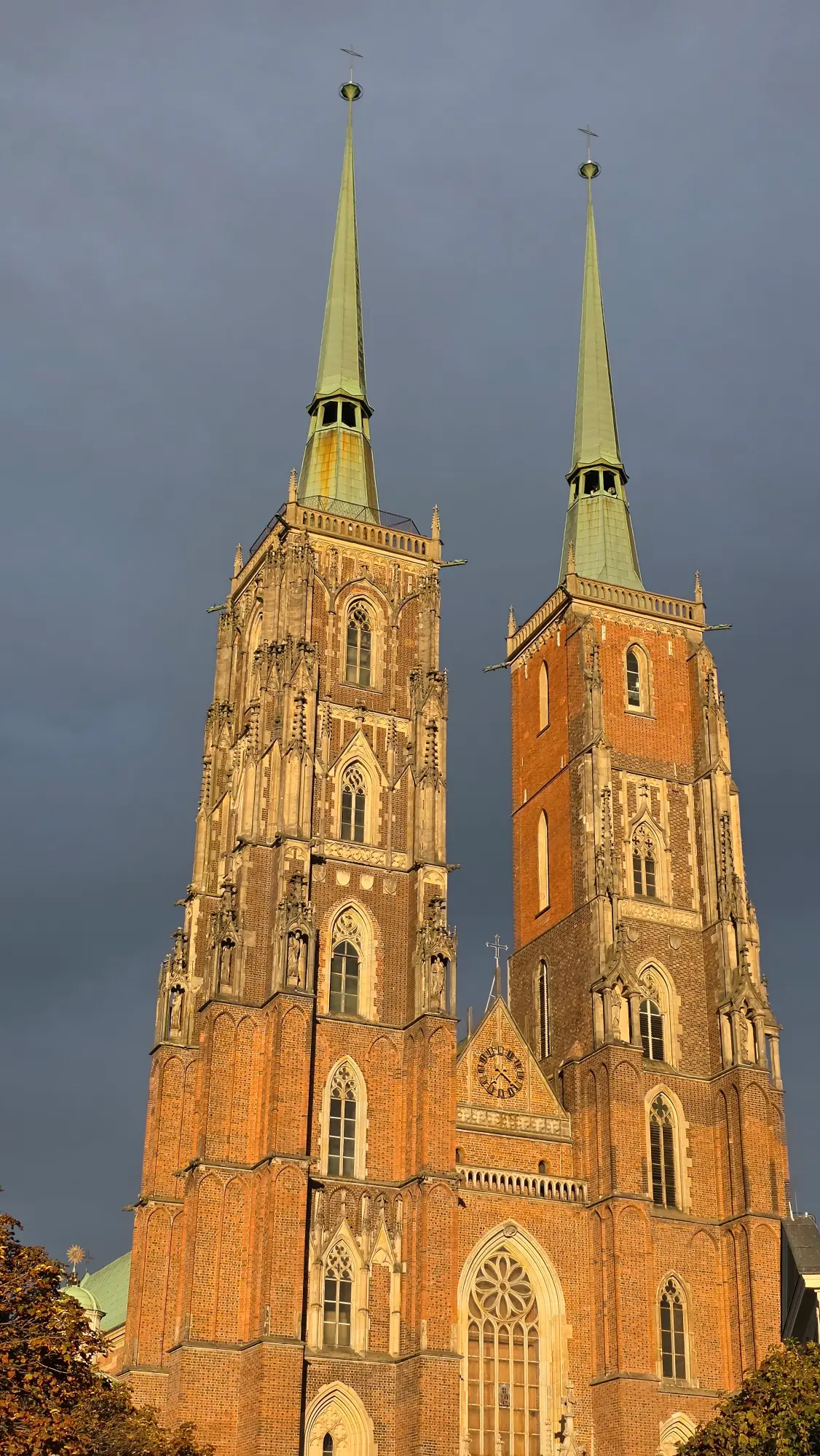 The two brick towers of Wroclaw Cathedral at sunset, set against a dark, dramatic sky.