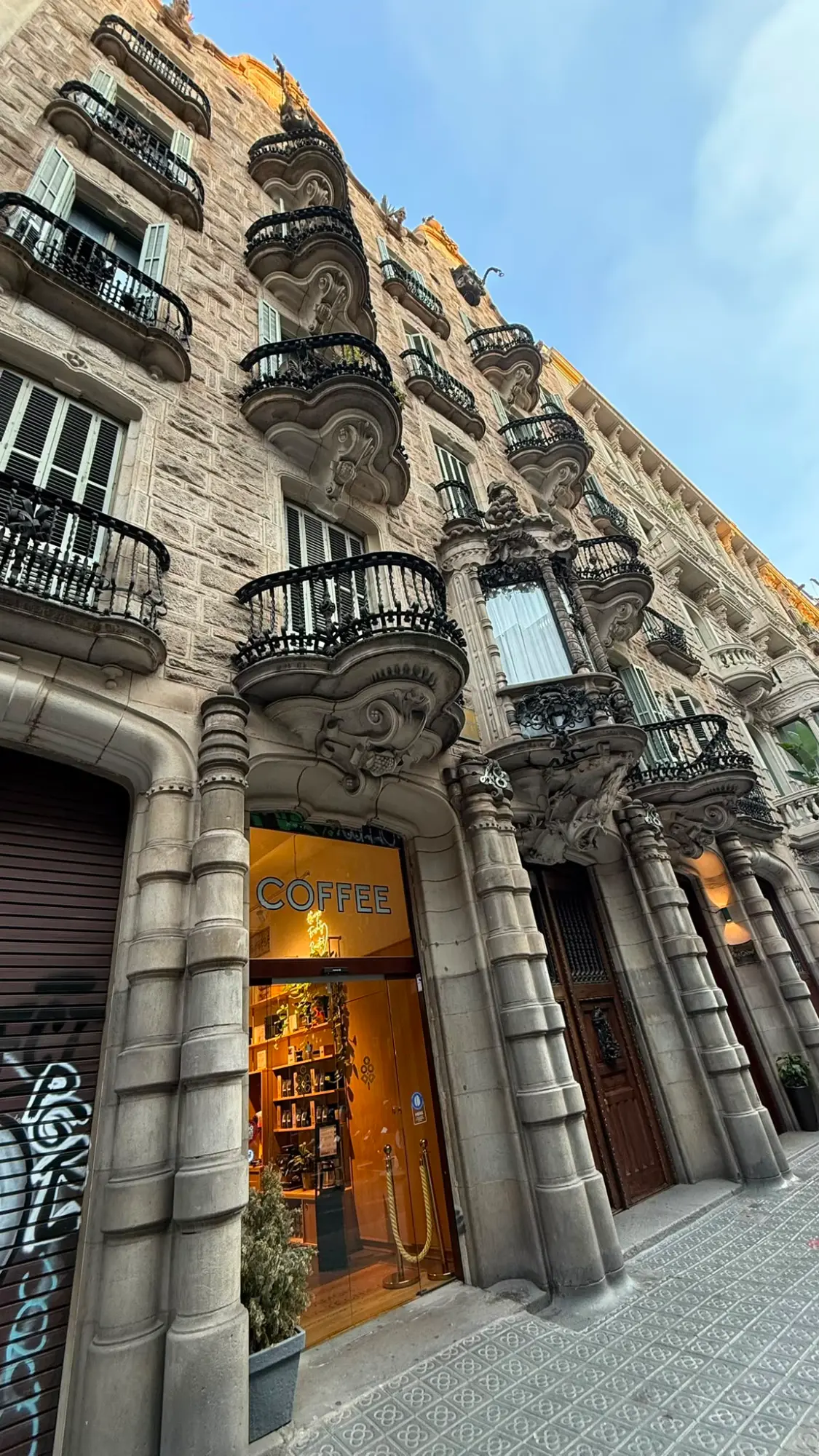 Stone facade of a building in Barcelona with ornate black wrought-iron balconies, seen from a low angle.