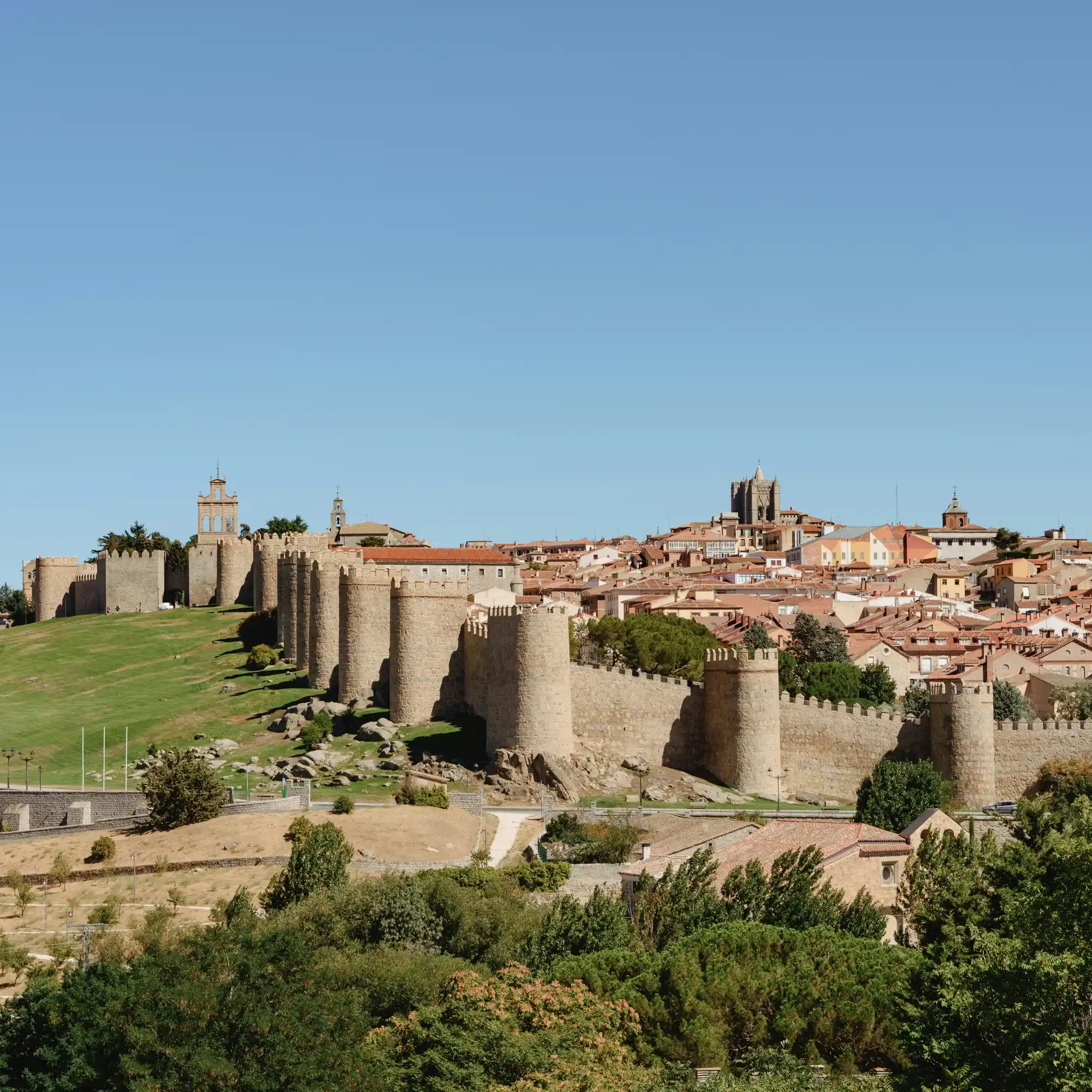 The medieval stone walls of Ávila, Spain, on a sunny day with the city visible behind them.