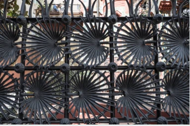 Close-up of a black wrought-iron fence with a repeating spiral fan-like pattern.