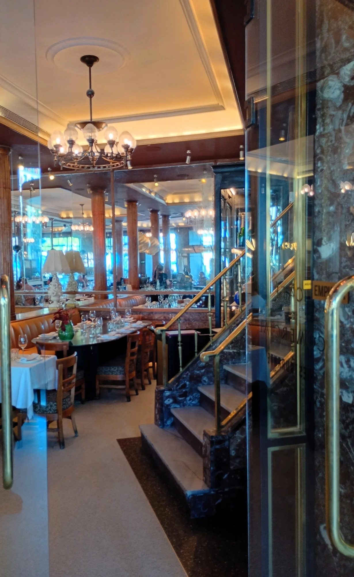 Elegant interior of the historic Café Comercial in Madrid, with tables, mirrors, and a marble staircase viewed from the en...