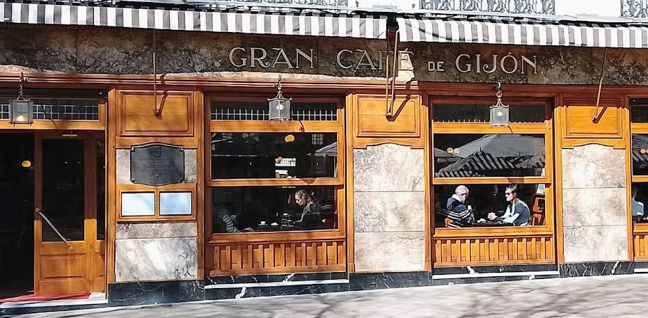 The classic wood and marble facade of the Gran Café de Gijón in Madrid, with patrons visible through the windows.
