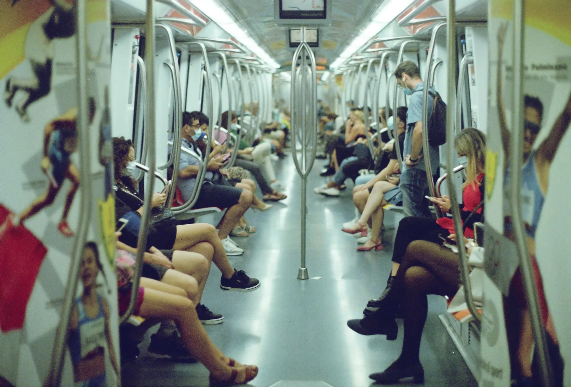 Interior view of a modern subway car with passengers seated on both sides, some wearing face masks.