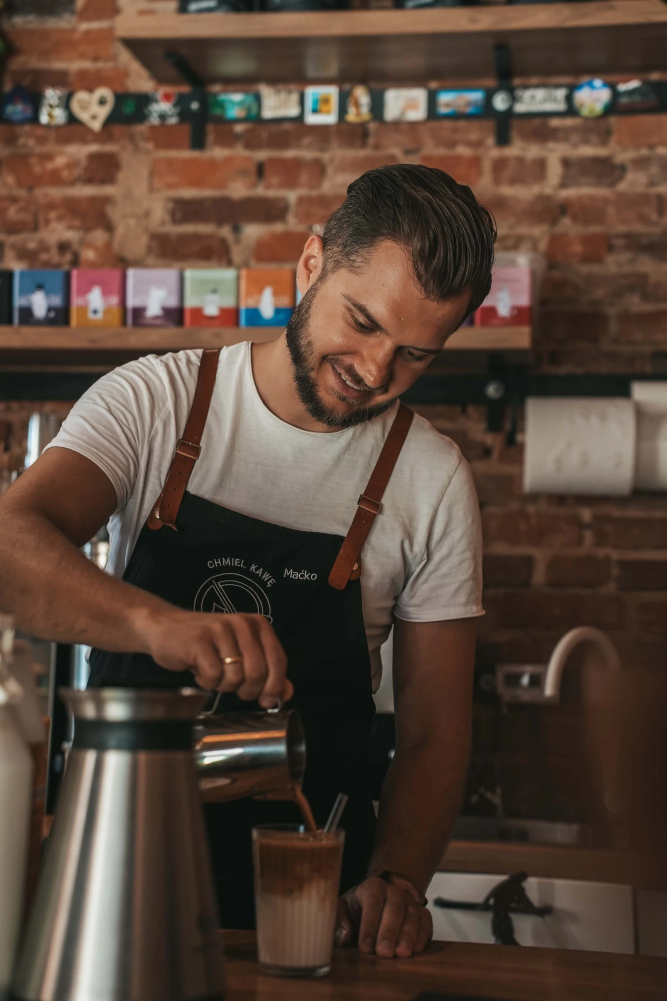 Uśmiechnięty barista z brodą w fartuchu z napisem