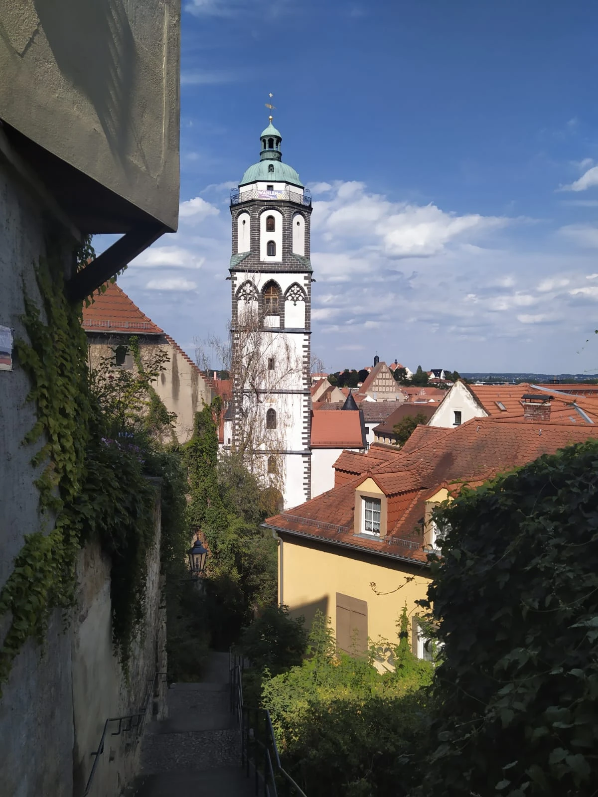 View from an alley at the Albrechtsburg castle tower and the red roofs of Meissen's old town under a blue sky.