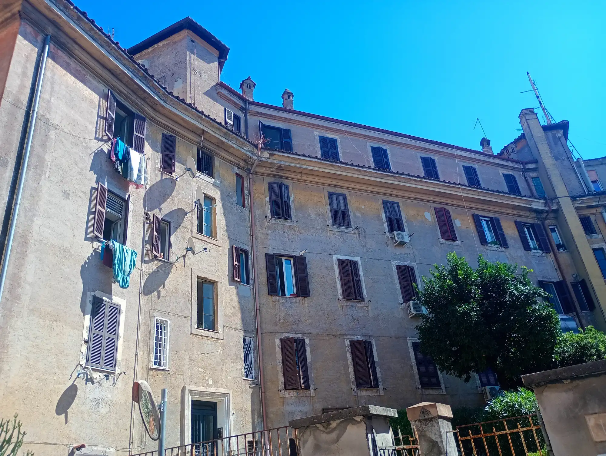 Multi-story Roman apartment building with dark shutters and laundry hanging from a window on a sunny day.