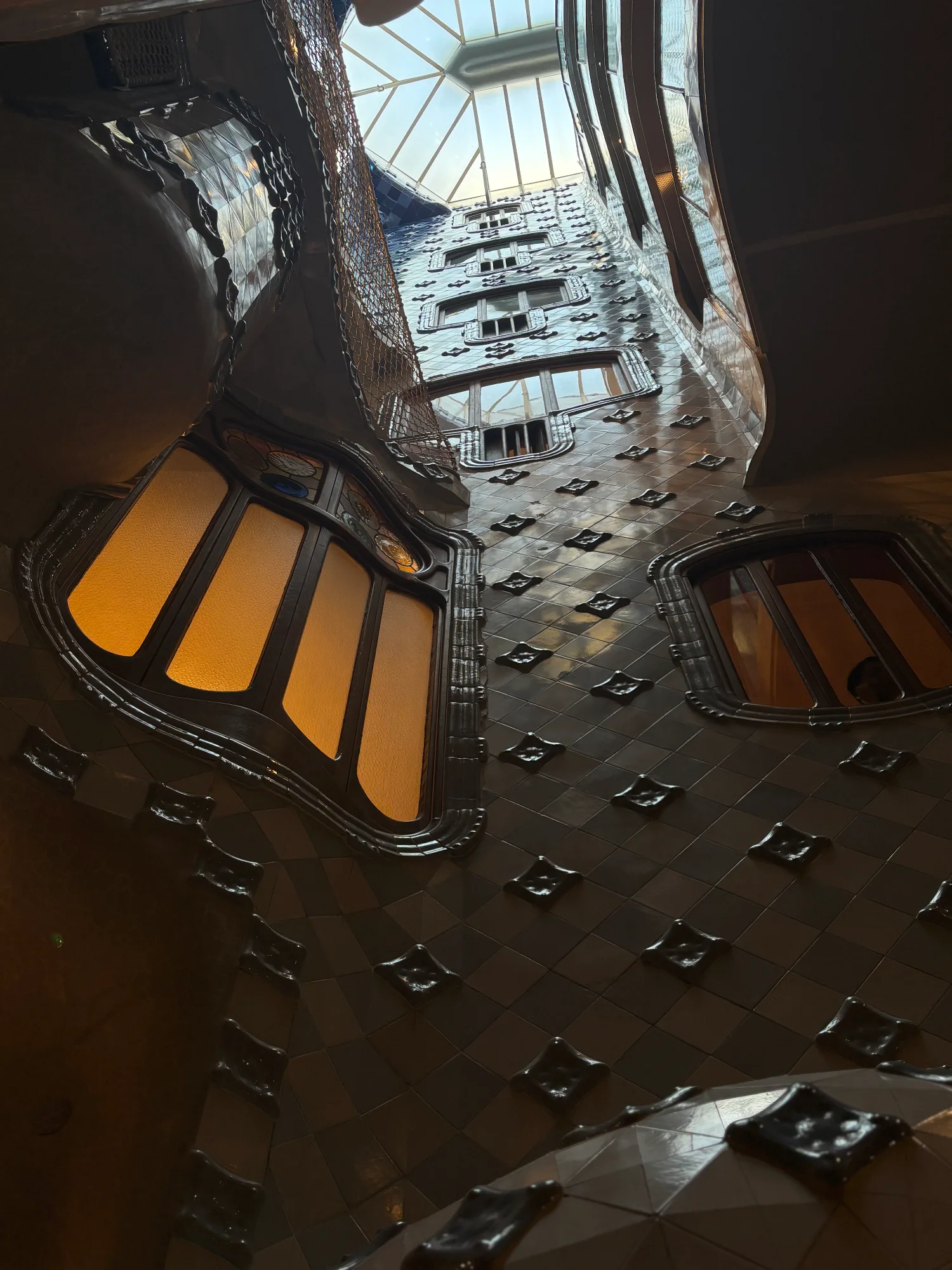 Looking up at the tiled interior courtyard of Casa Batlló, with its wavy walls and a skylight at the top.
