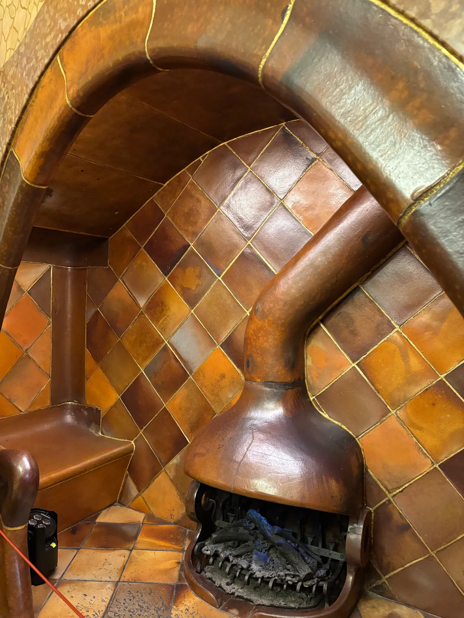 A unique mushroom-shaped fireplace with a copper-colored finish inside a tiled alcove at Casa Batlló.