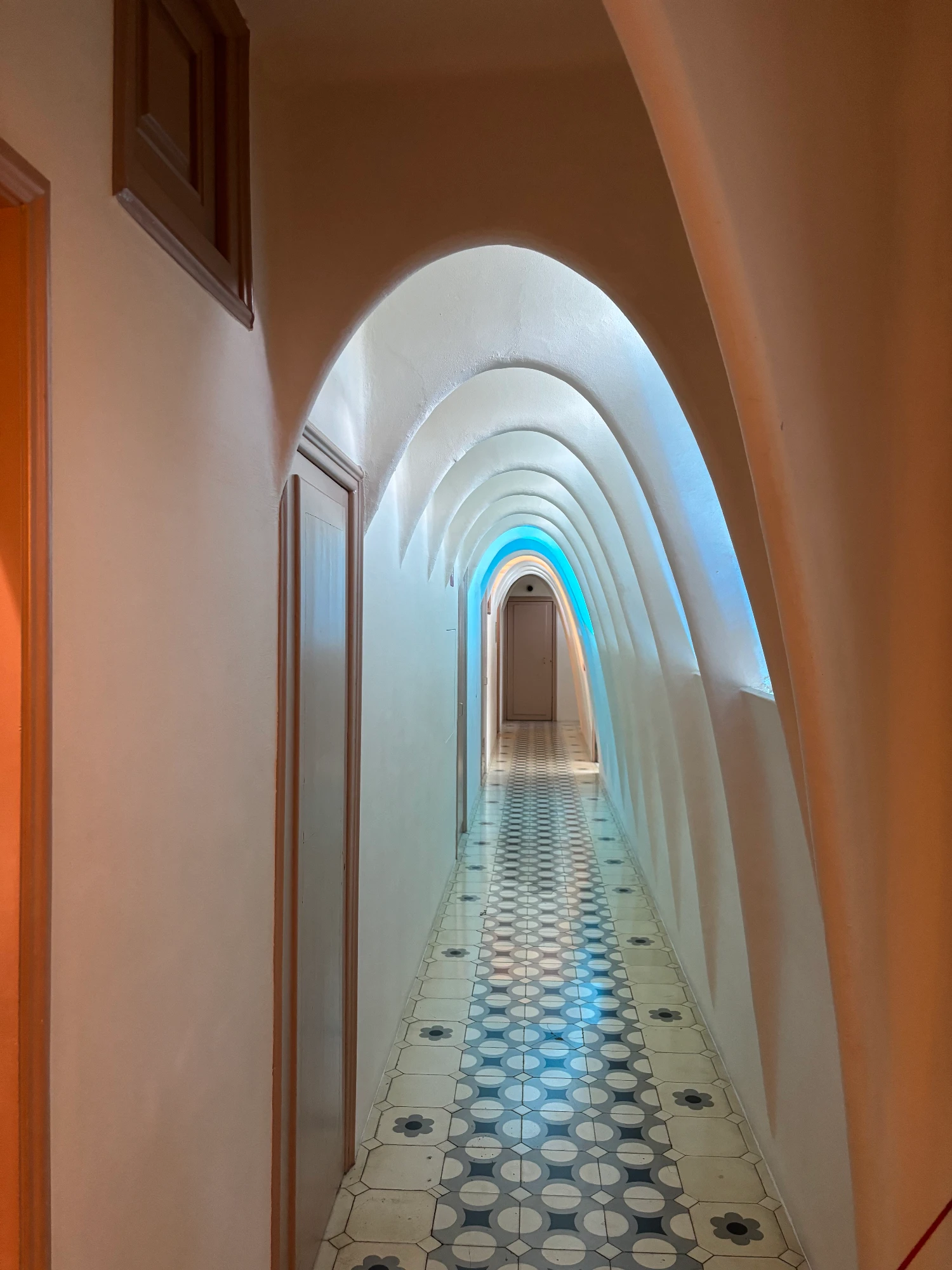 Long corridor with a tiled floor and a ceiling of white, repeating arches inside Gaudí's Casa Batlló building.