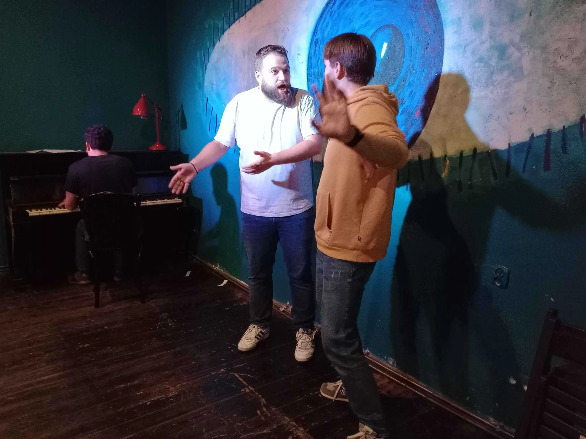 Two men singing or acting enthusiastically while a man plays the piano in the background.