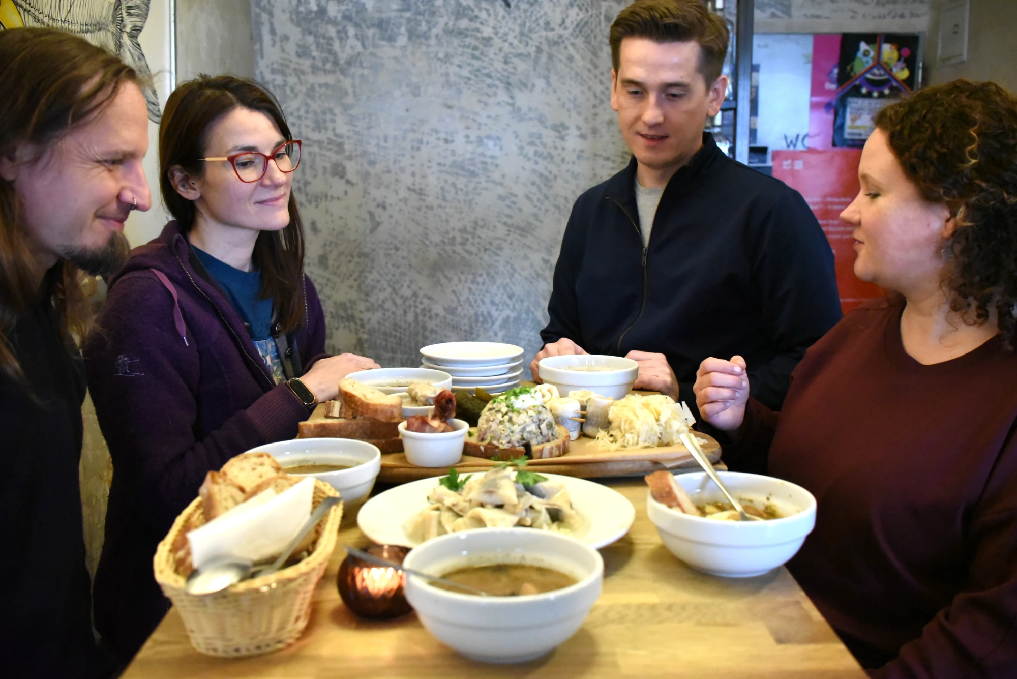 Four people sitting at a table in Krakow, sharing traditional Polish dishes like herring, bread, and soup.