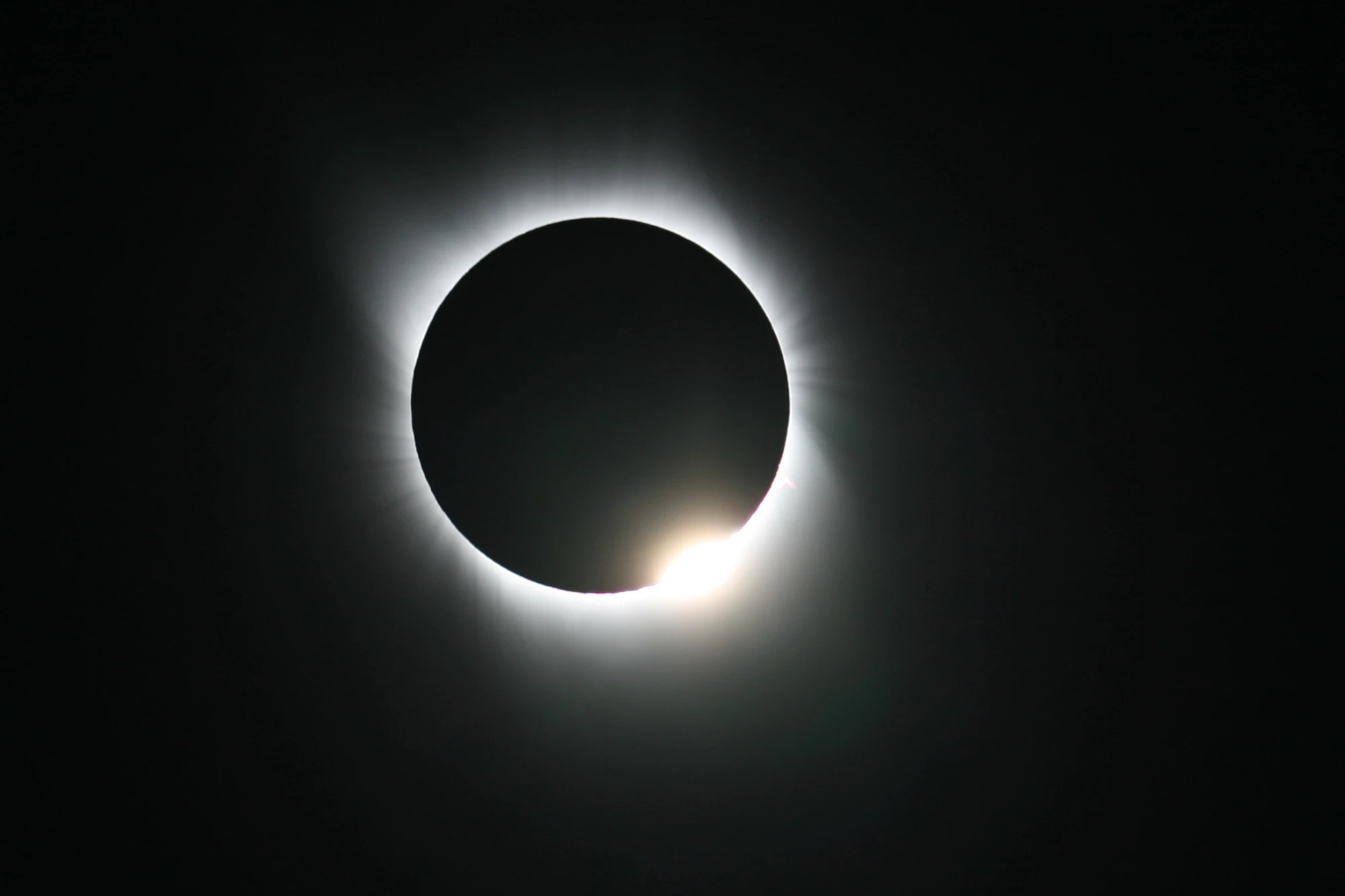 A total solar eclipse showing the diamond ring effect, where one bright spot of light bursts from the edge of the moon.