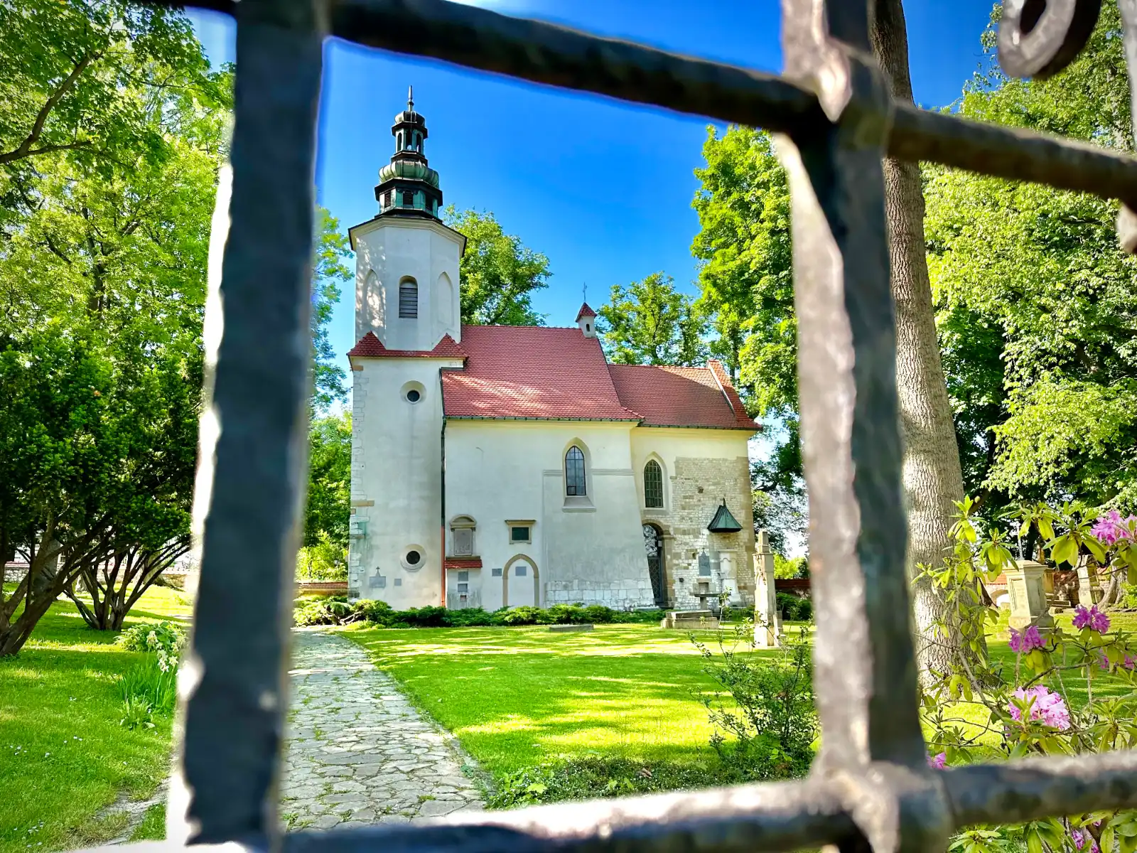 St. Salvator's Church in Krakow, a small white building with a red roof, viewed through the bars of an iron gate on a sunn...