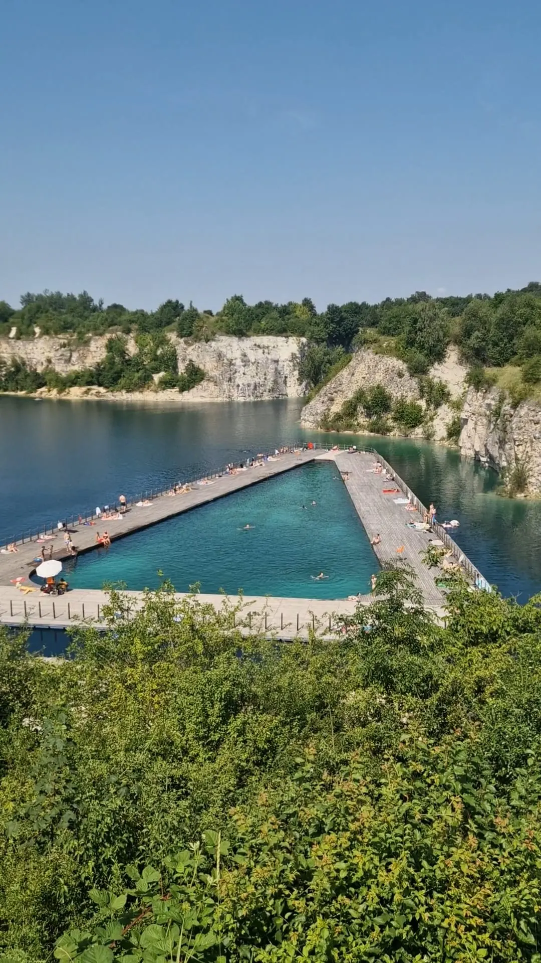 Floating swimming pools at the Zakrzówek quarry on a sunny day, surrounded by cliffs and trees.
