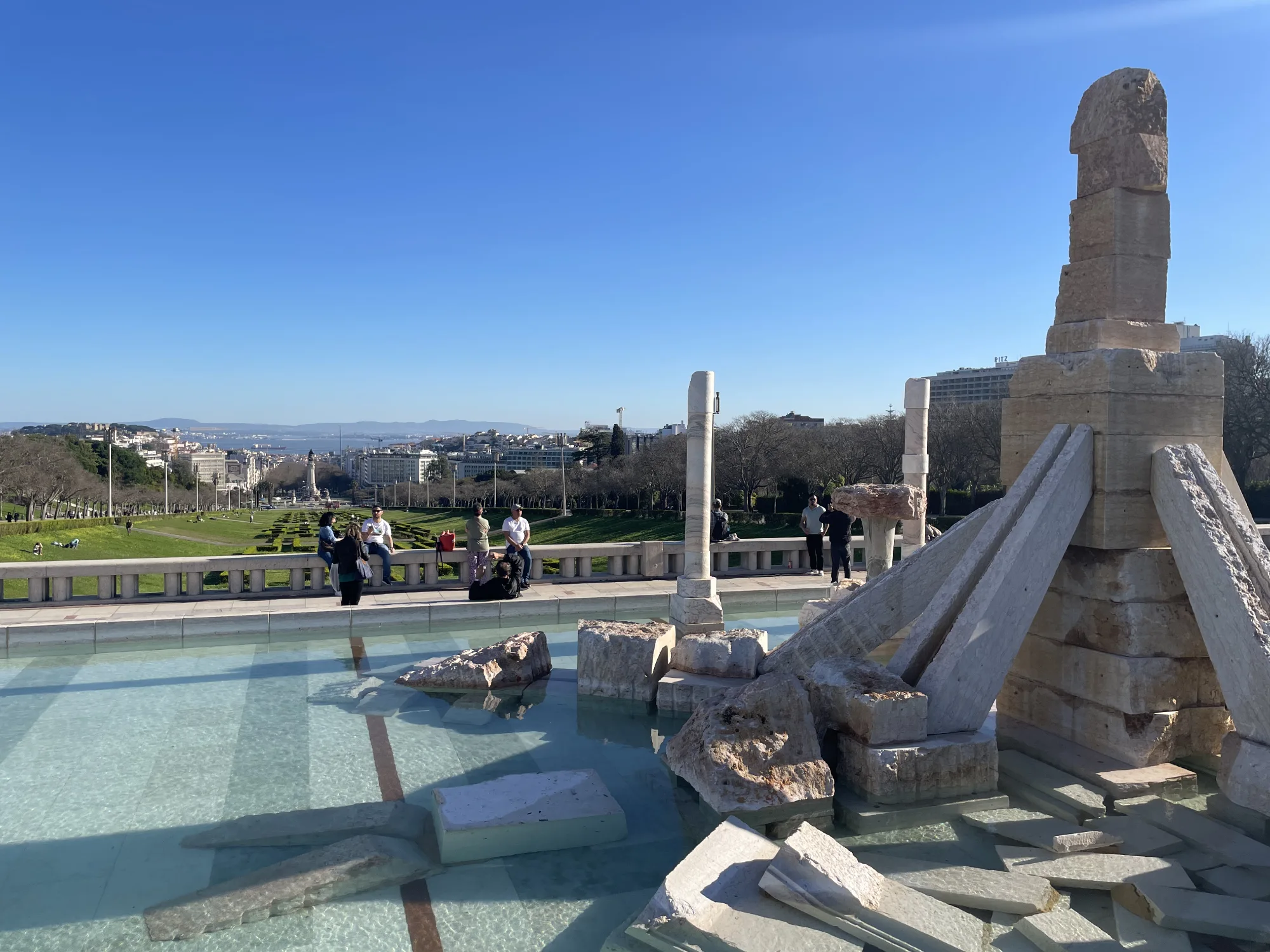 Stone monument in a pool at Eduardo VII Park, overlooking Lisbon's cityscape and the Tagus River.