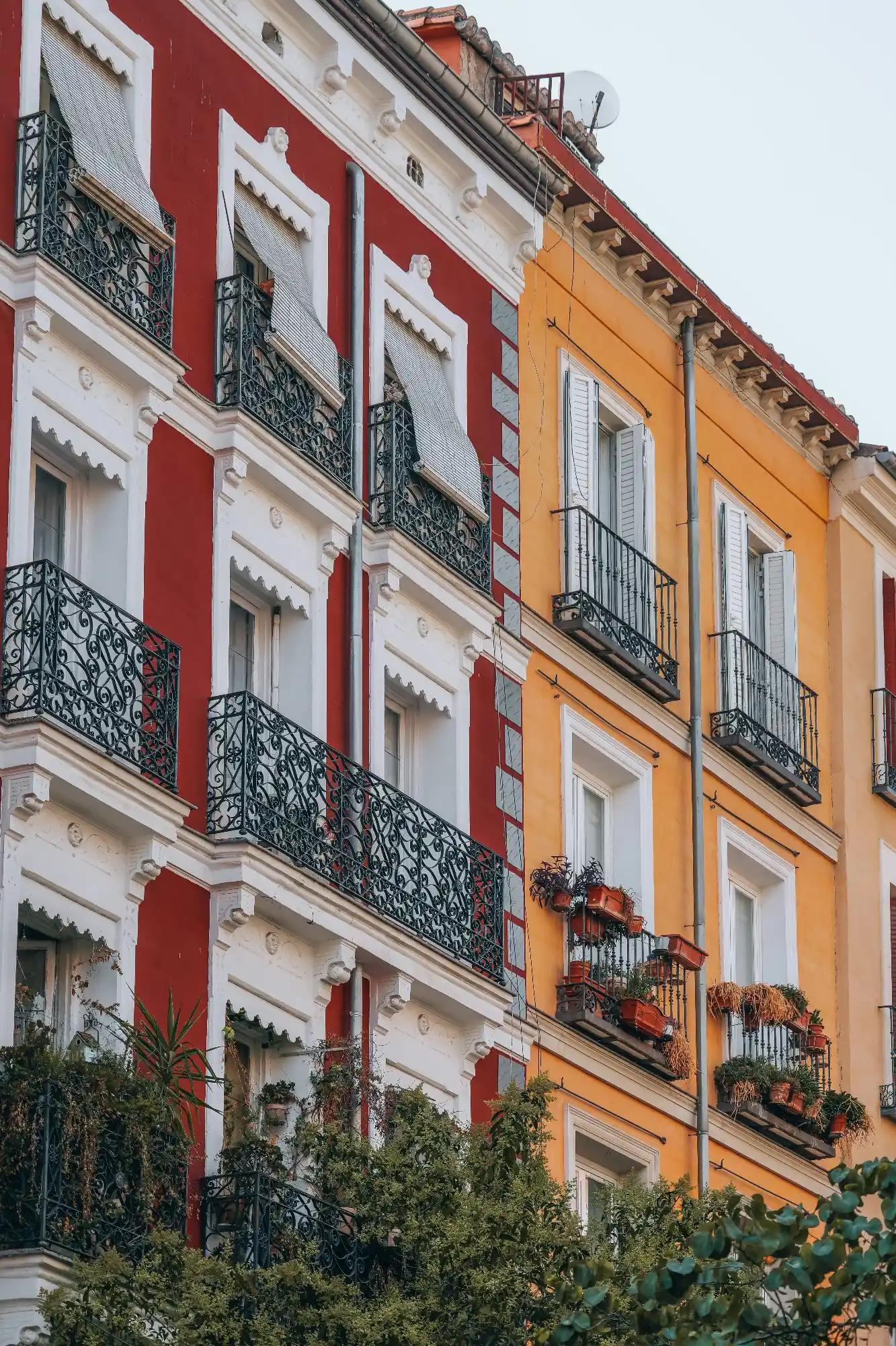 A red and an orange apartment building side-by-side, with ornate black metal balconies and white window frames.