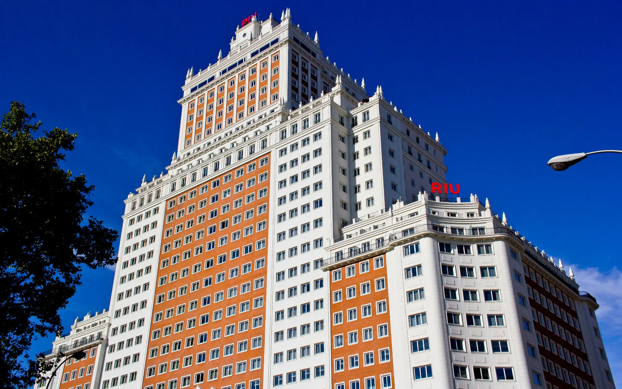 The grand facade of the historic Edificio España, now the Hotel Riu, against a clear deep blue sky in Madrid.