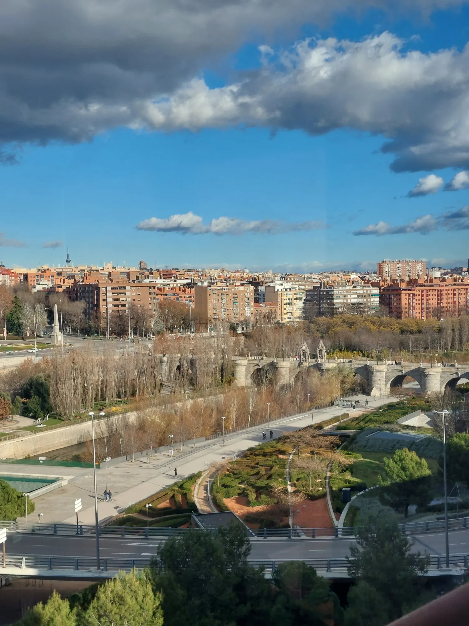 Widok na rzekę Manzanares w Madrycie, z zabytkowym mostem Puente de Toledo i budynkami miasta pod częściowo zachmurzonym n...