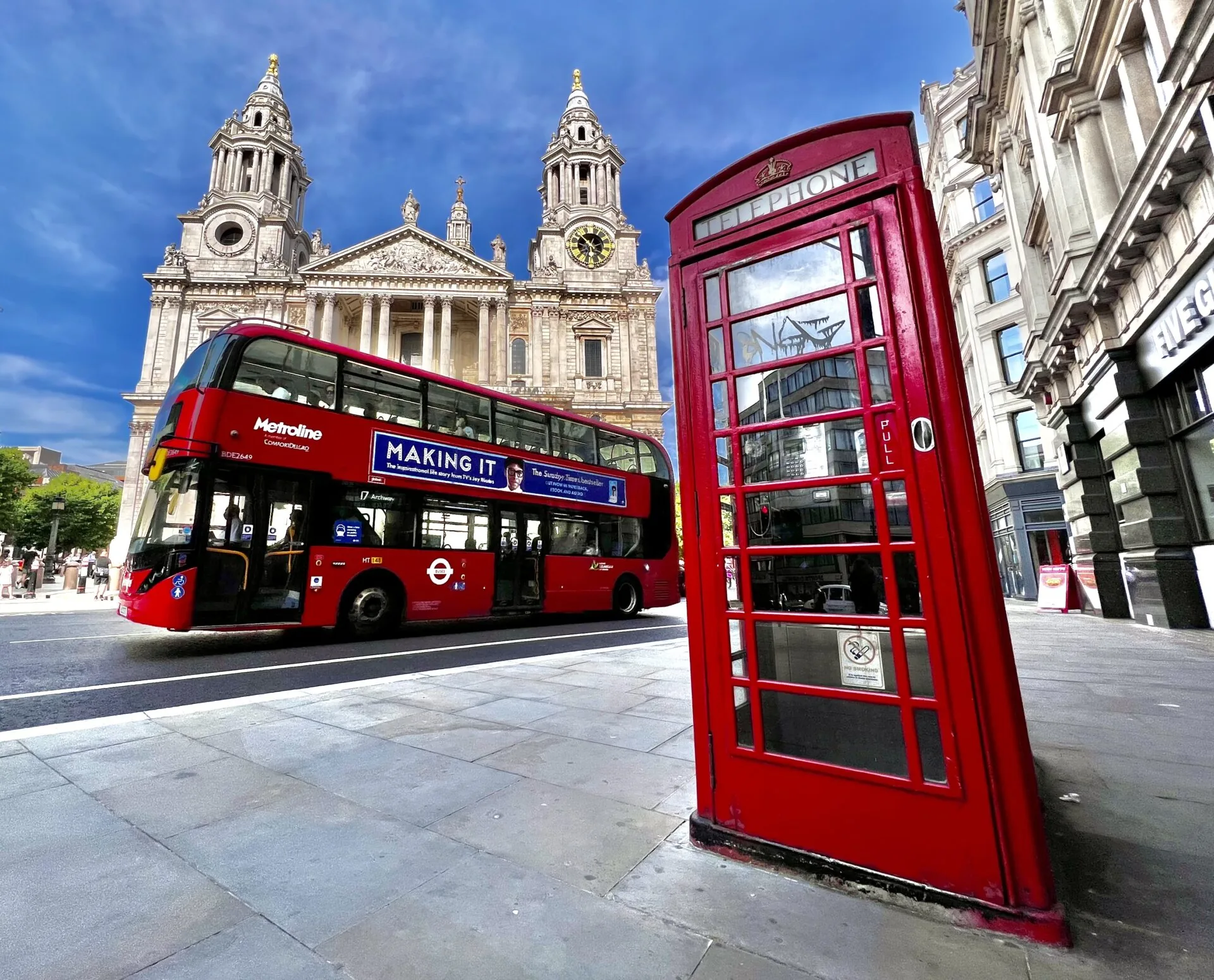 Catedral de San Pablo detrás de un autobús rojo de dos pisos y una cabina telefónica roja en una calle soleada de Londres.