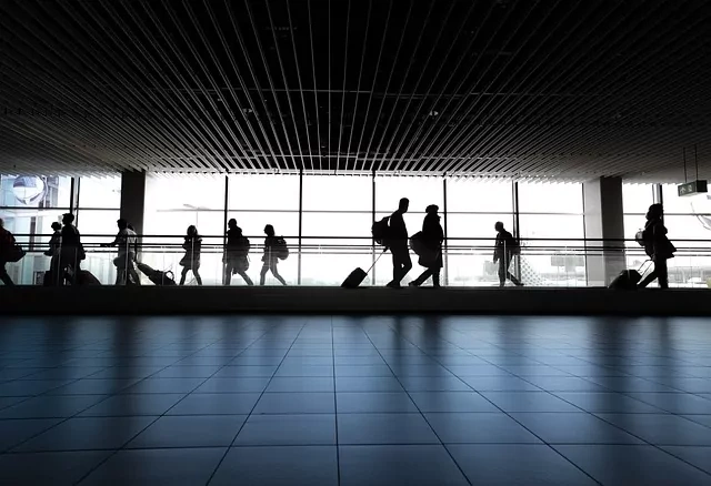 Silhouettes of passengers on a moving walkway in a modern airport terminal with large windows.