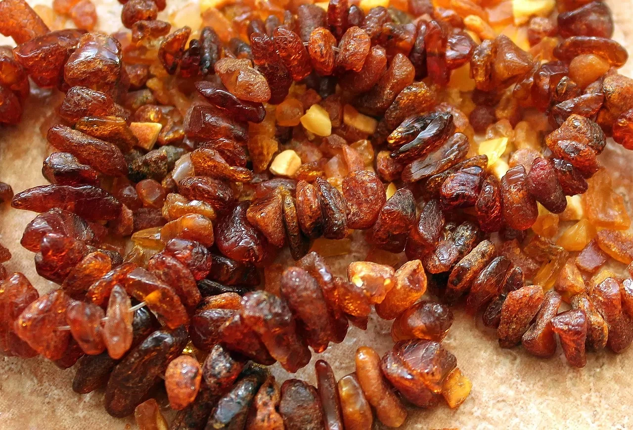 Close-up of numerous small, irregular amber pieces and beaded jewelry in various shades of brown and orange.