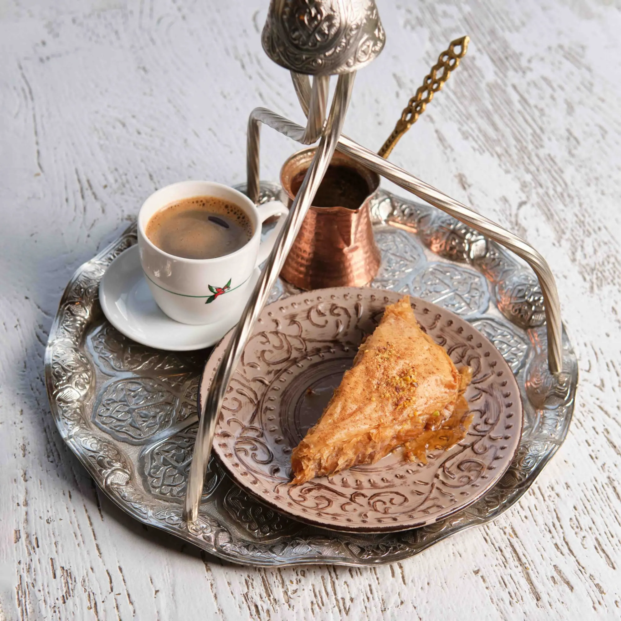 Silbernes Tablett mit einer Tasse Kaffee, einem Kupfer-Cezve, einem goldenen Löffel und einem Stück Baklava auf einem gemuste