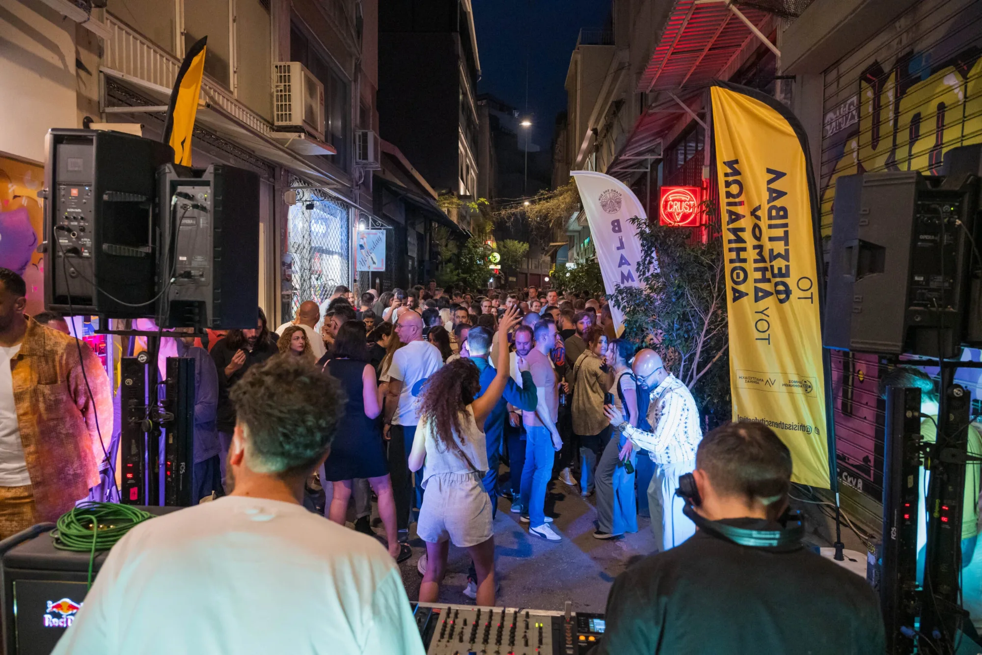 A DJ plays music for a crowd of people dancing at a street party in a narrow city alley at night.
