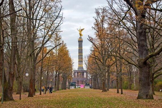 The Berlin Victory Column (Siegessäule) at the end of a tree-lined avenue in Tiergarten during autumn, with fallen leaves and