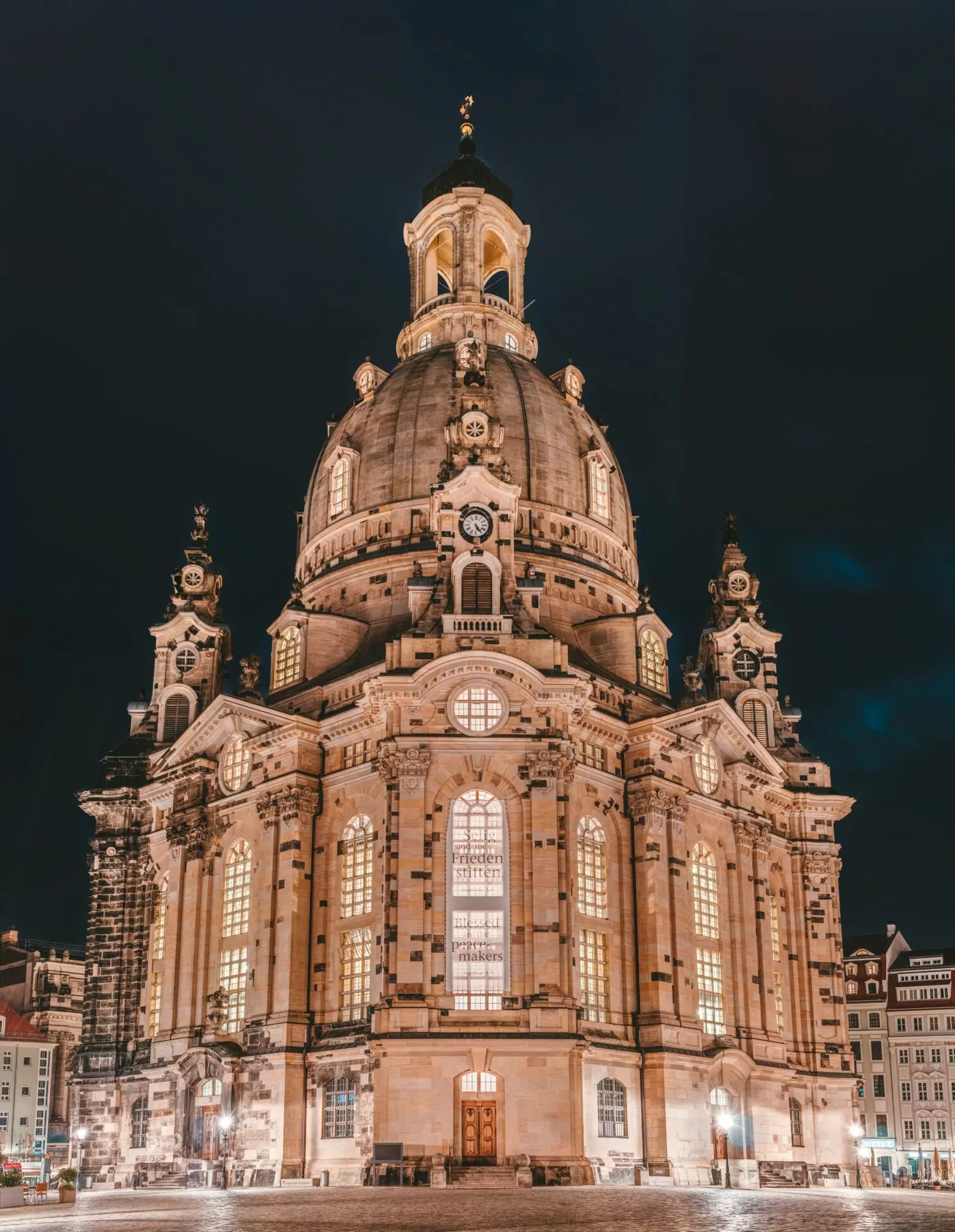 Dresden Frauenkirche at night, showing its domed roof, illuminated windows, and surrounding buildings under a dark sky.