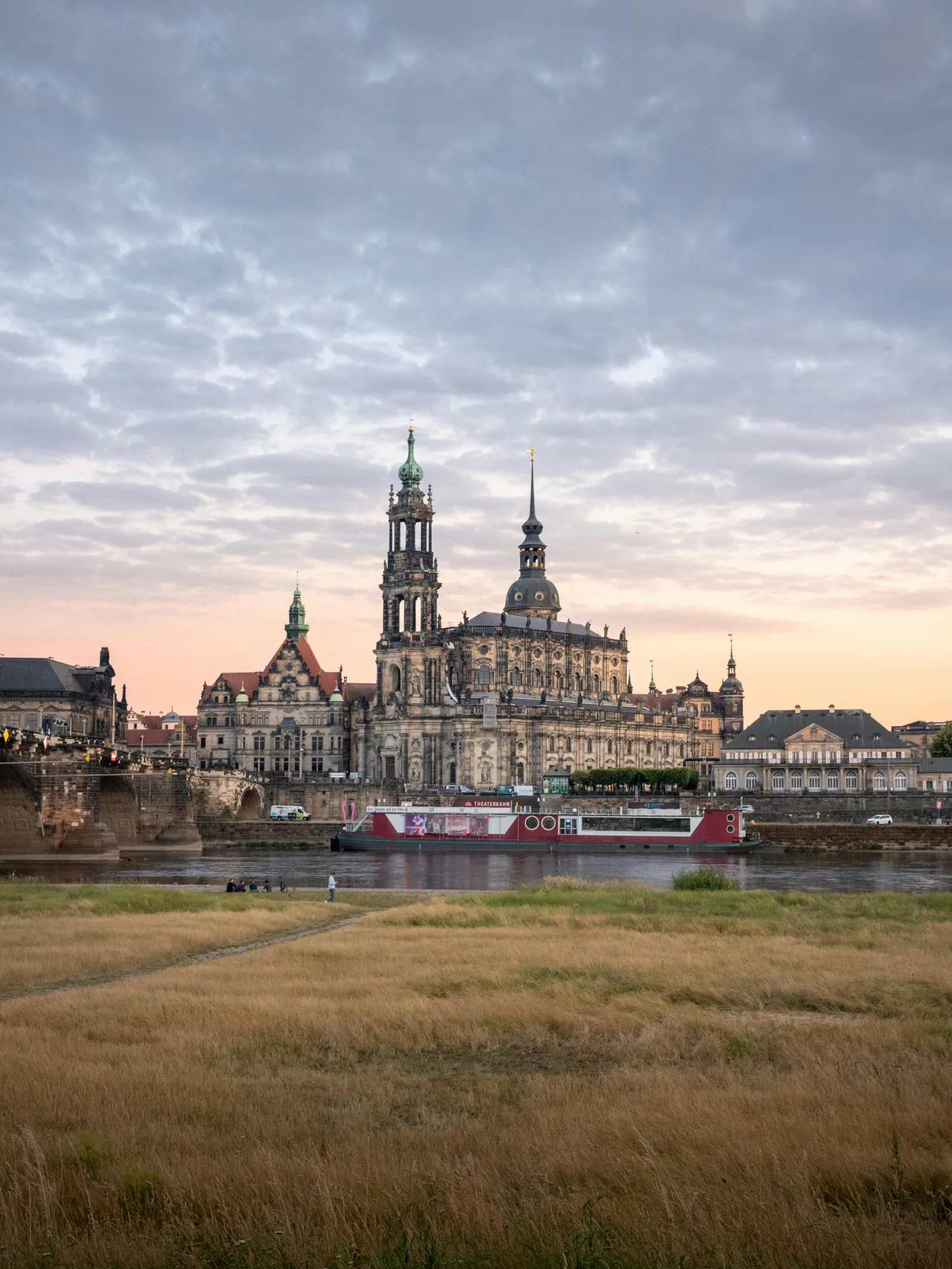 Baroque Hofkirche and other historic buildings along the Elbe River in Dresden under a cloudy sky.