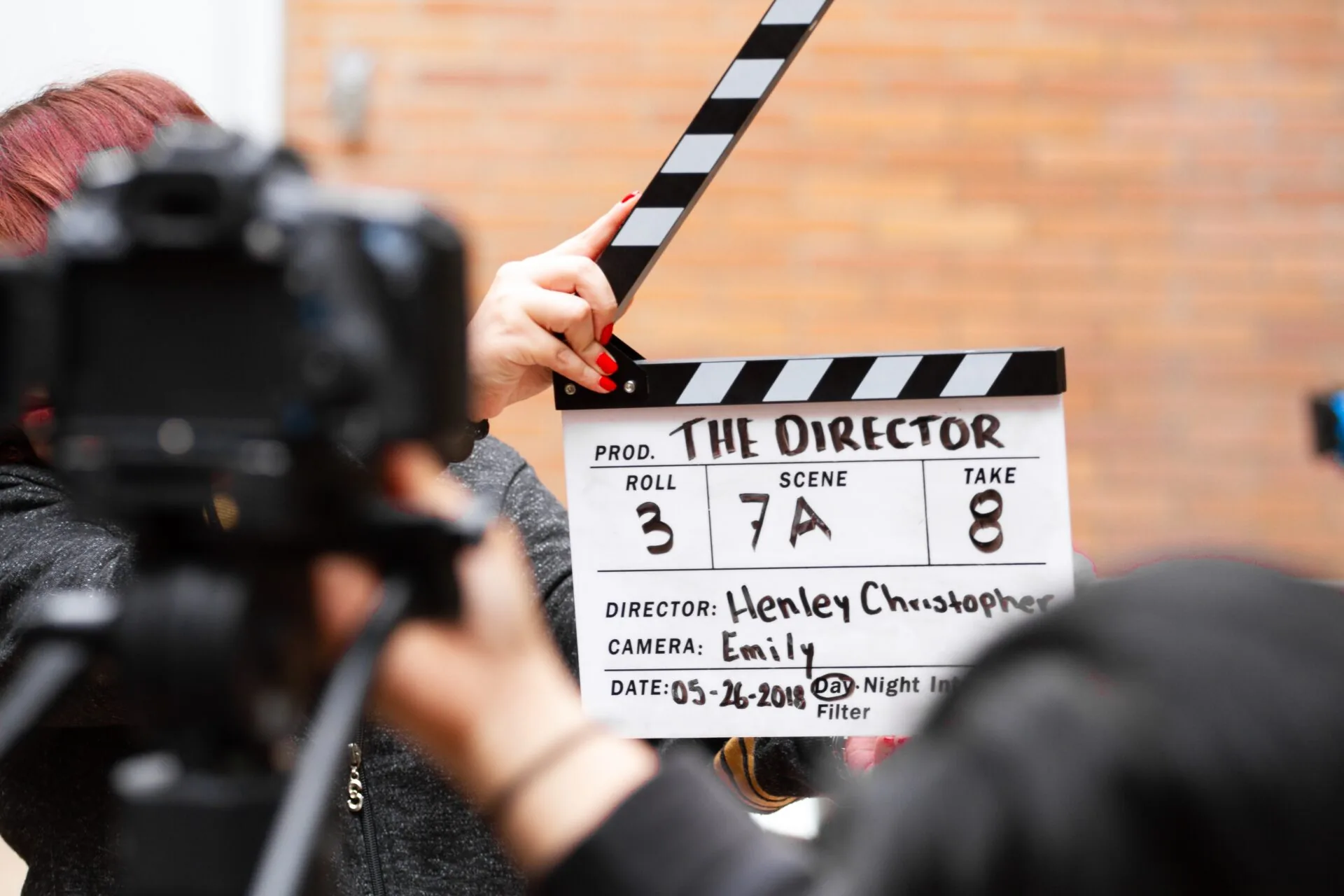 A person holds open a film clapperboard in front of a camera, with the title 'THE DIRECTOR' visible.