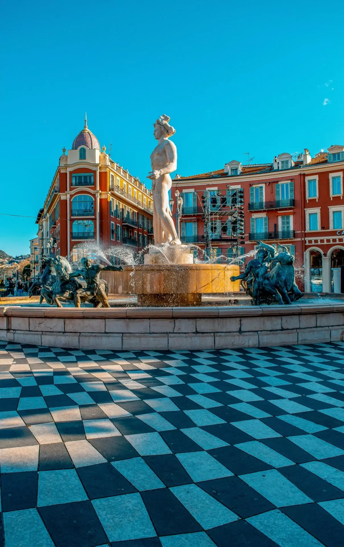 Fontaine du Soleil (Apollo Fountain) in Place Massena, Nice, with water spraying and checkered pavement in foreground.