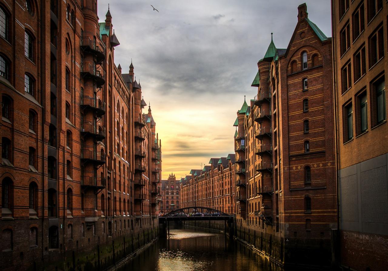 Historic brick warehouses with green roofs line a canal at sunset in Hamburg's Speicherstadt district.