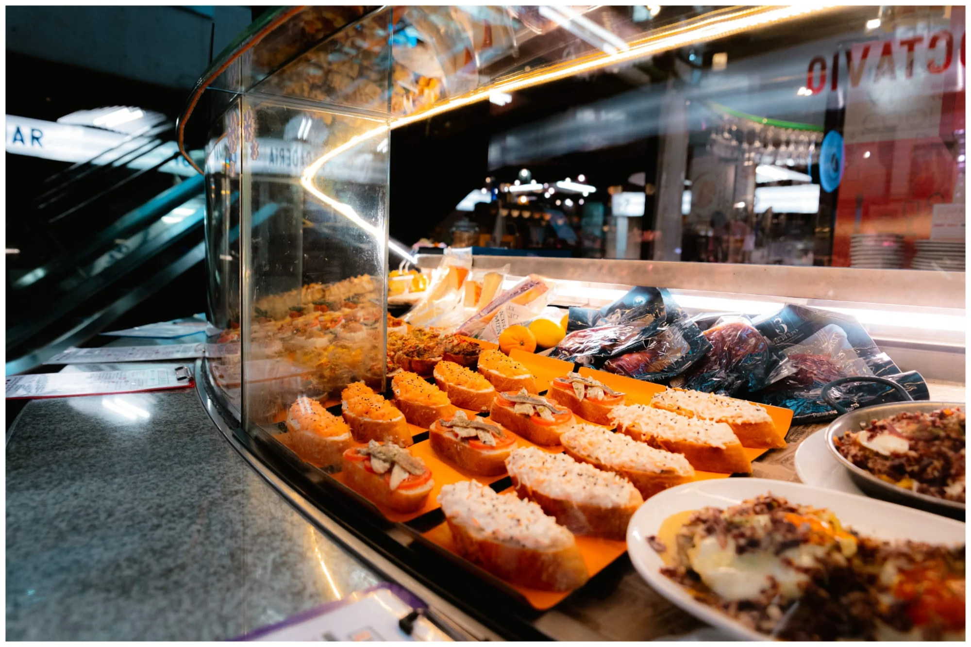 A variety of Spanish tapas and pinchos on bread slices, arranged inside a brightly lit glass display counter.