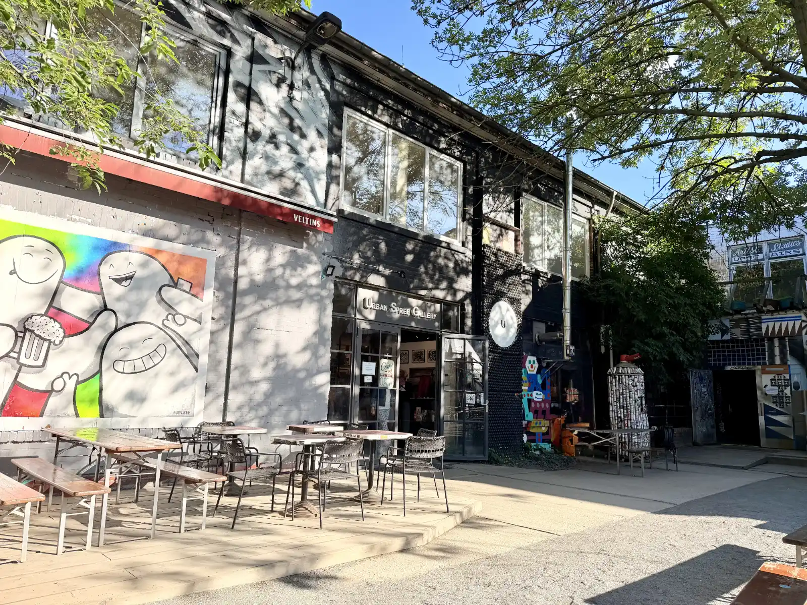 Innenhof der Urban Spree Galerie in Berlin mit Street Art, Tischen im Freien und dem Galerieeingang.