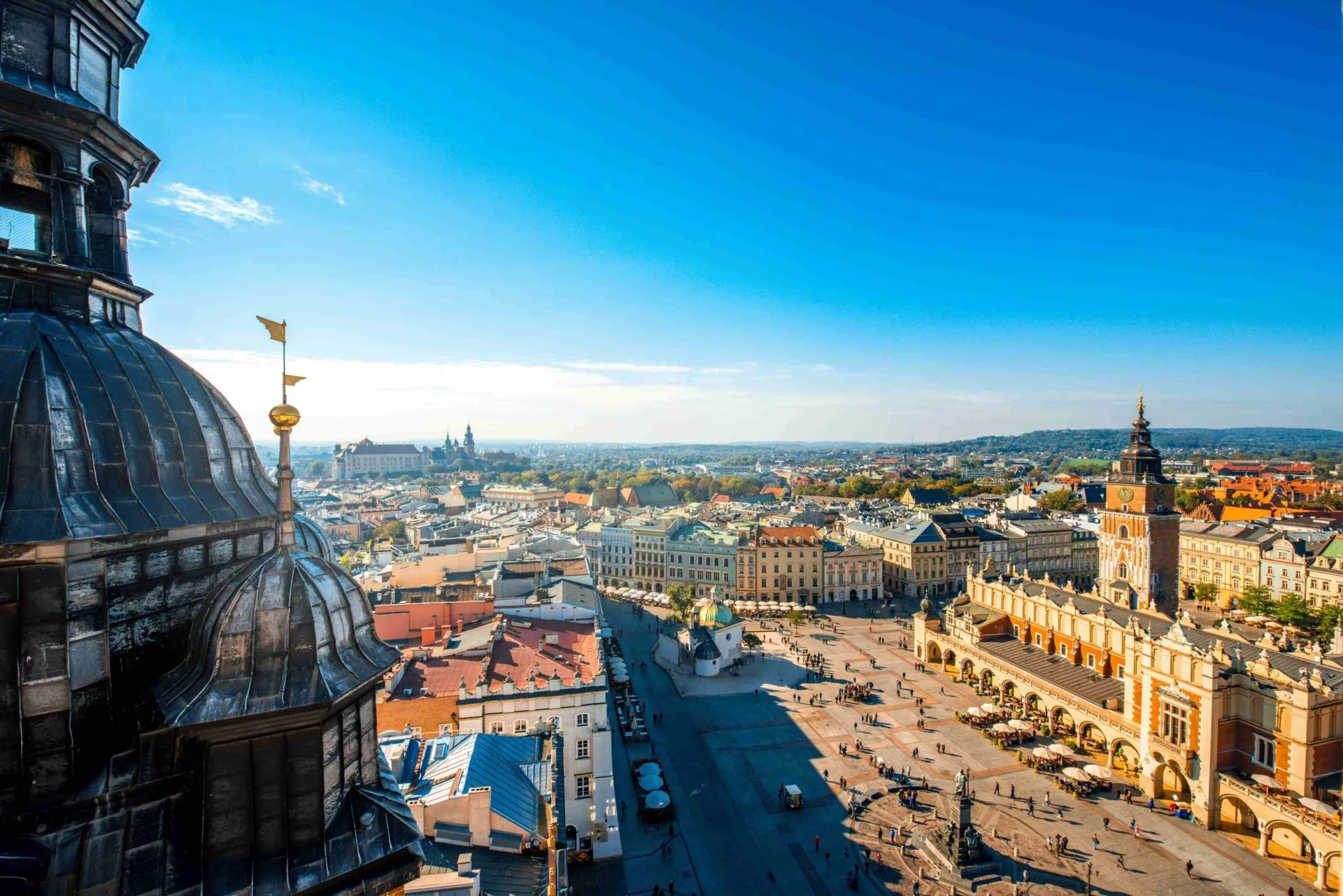 Widok z góry na Rynek Główny w Krakowie z Sukiennicami, wieżą Bazyliki Mariackiej i Zamkiem Wawelskim w tle.