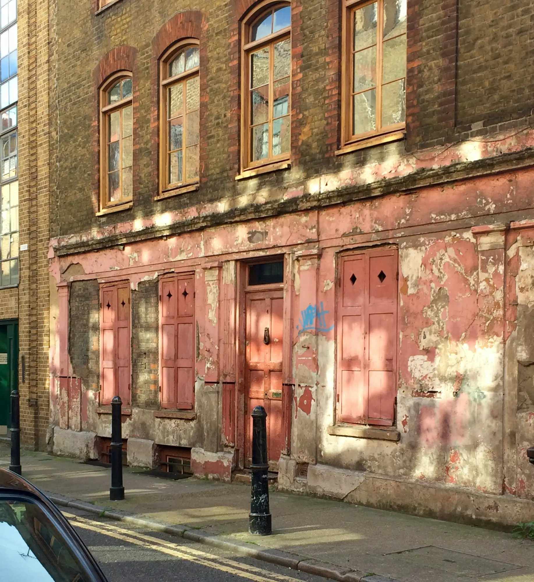 A weathered brick building with a faded pink ground-floor storefront, viewed from a street in London.