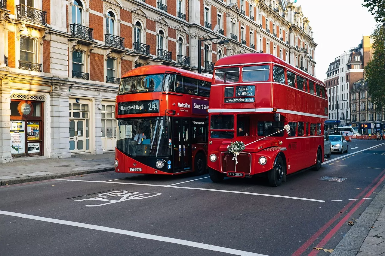 Two red London double-decker buses on a street, one modern and one vintage decorated for a wedding.