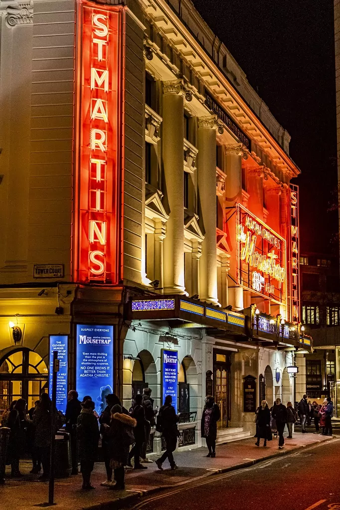 Exterior del St Martin's Theatre en Londres de noche, con letreros de neón rojos, columnas clásicas y gente en la acera.