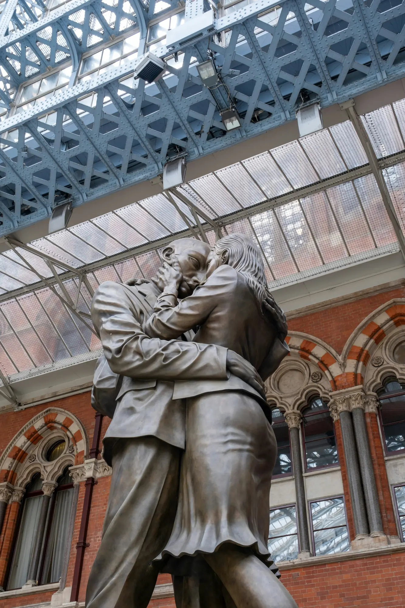 Una estatua gigante de bronce de un hombre y una mujer abrazándose bajo el techo de cristal de la estación de St Pancras.