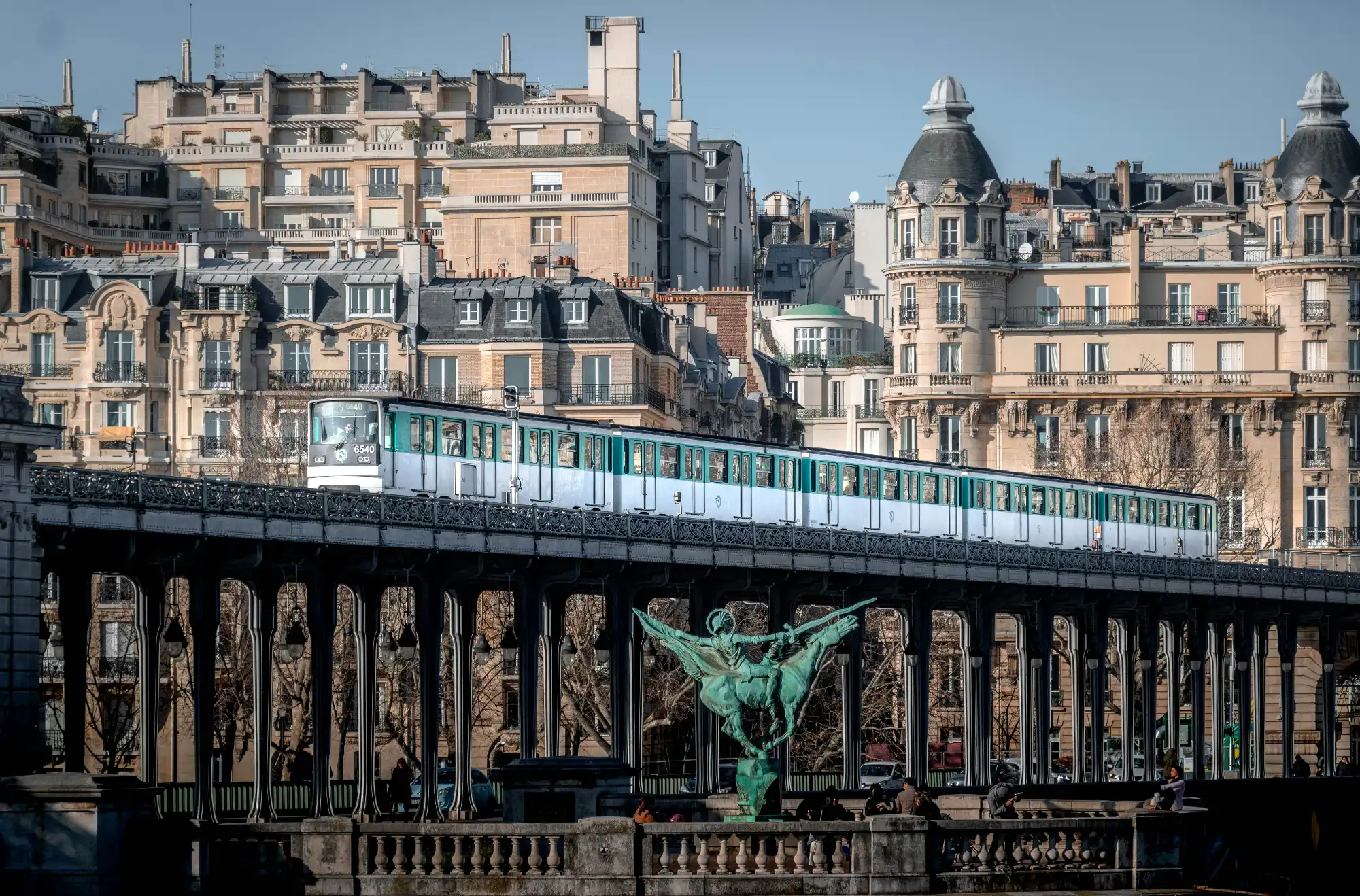A Paris Métro train crosses the Pont de Bir-Hakeim bridge, with a backdrop of classic Parisian buildings.