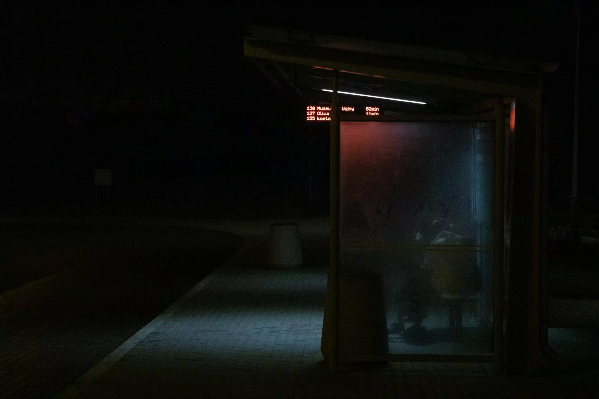 Przystanek autobusowy w nocy z cyfrowym wyświetlaczem pokazującym numery autobusów, kierunki i czasy odjazdu.