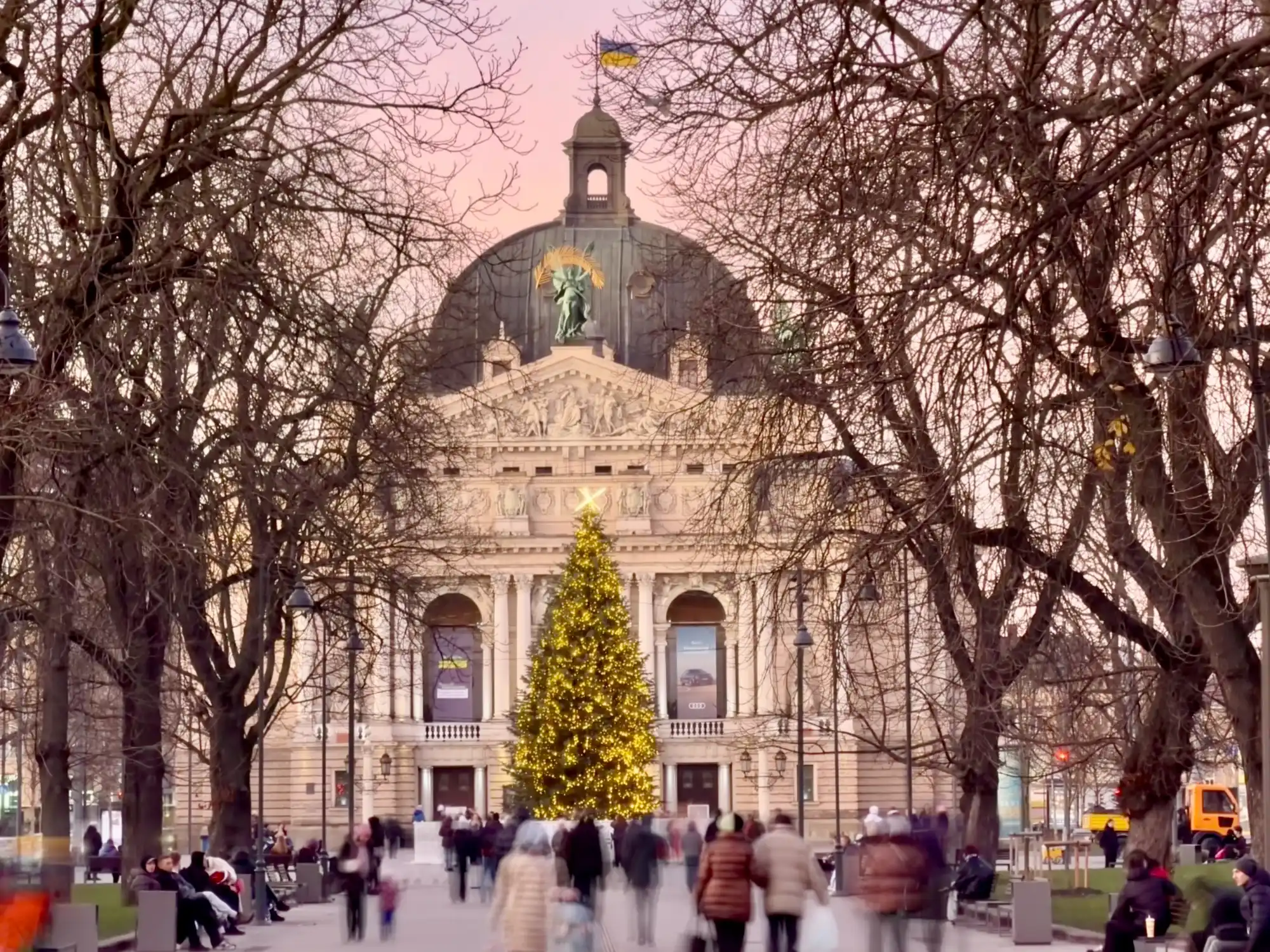 Lviv Opera House at dusk with a large glowing Christmas tree and an anti-tank obstacle star on top.